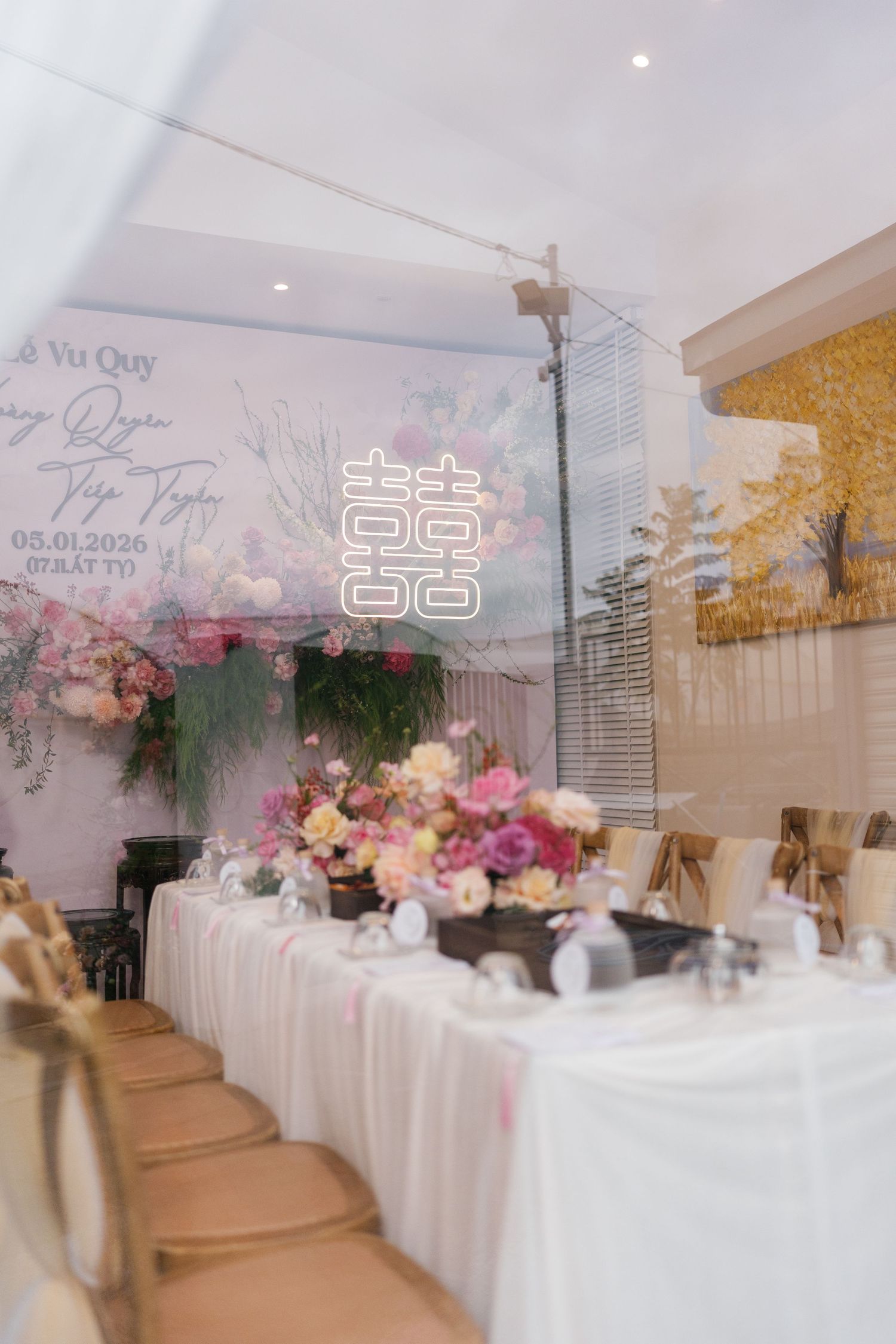 Elegant Vietnamese wedding reception with floral arrangements, white draped tables, double happiness neon sign, and decorative backdrop.