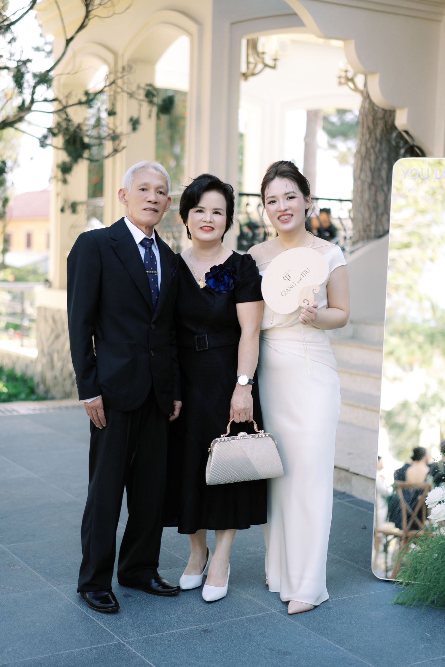 Elegant Asian family portrait with elderly couple and woman in white dress at wedding venue.