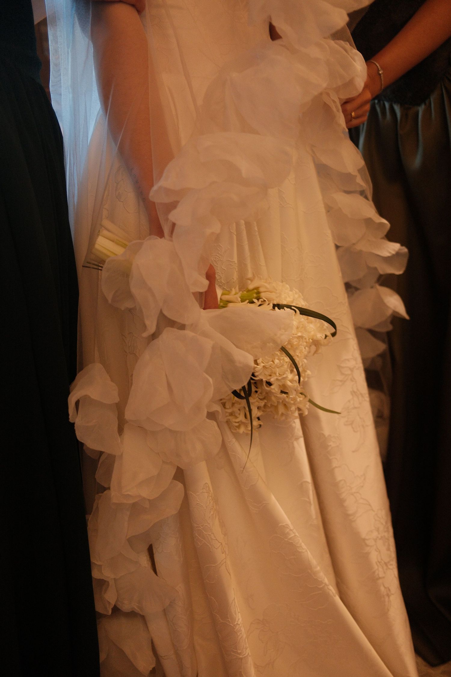 Close-up of a bride in a ruffled white wedding gown holding a delicate white floral bouquet.