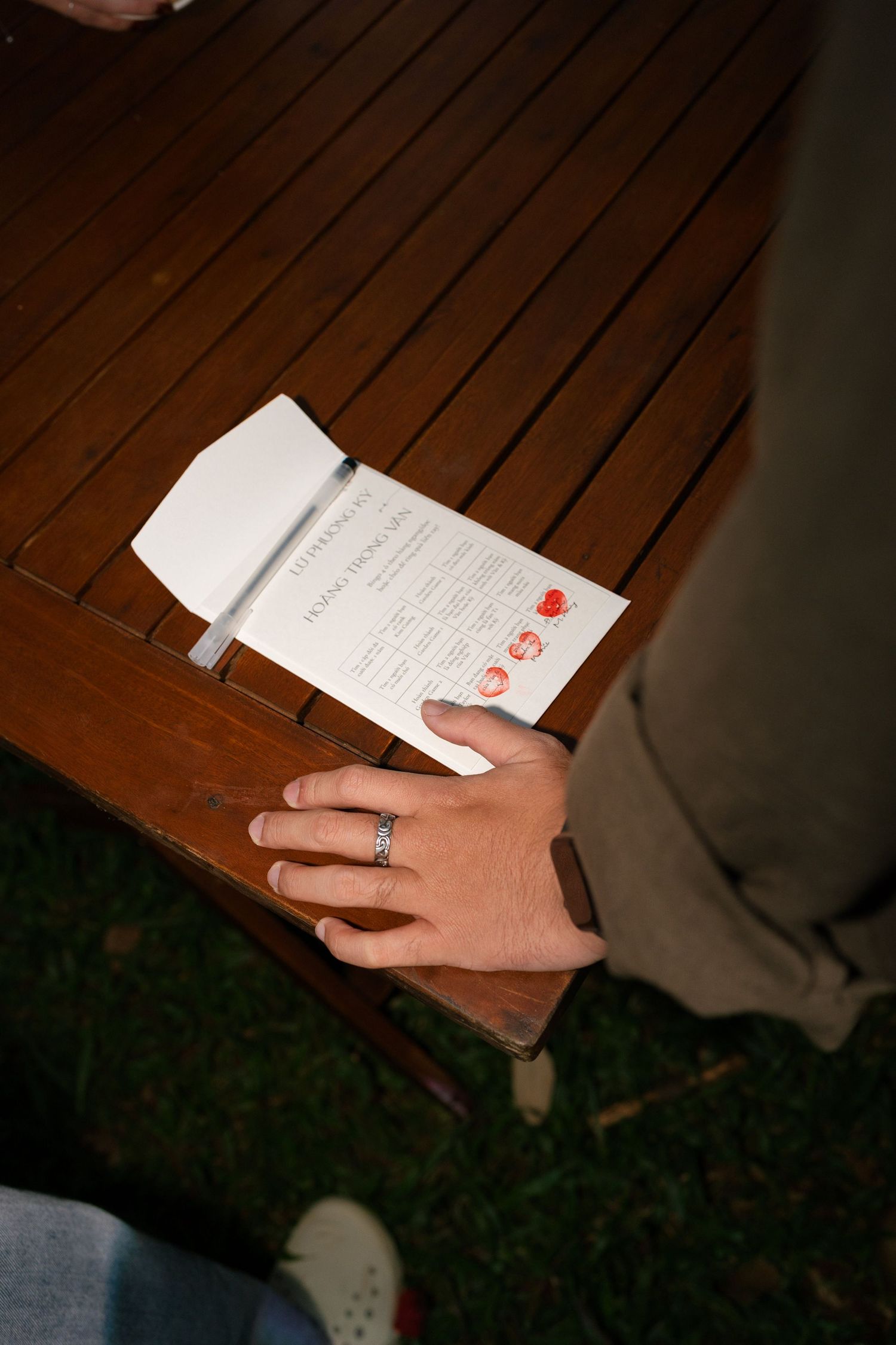 Close-up of hands holding a wedding program on a wooden table with a silver ring visible.