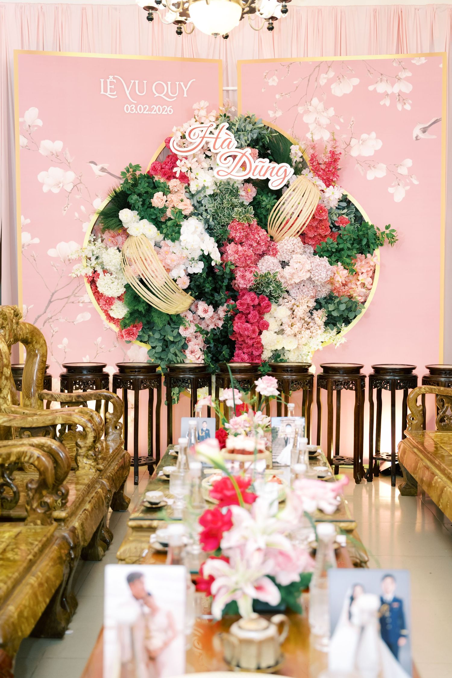 Elegant Vietnamese wedding reception with pink floral backdrop, ornate golden furniture, and decorated dining tables.