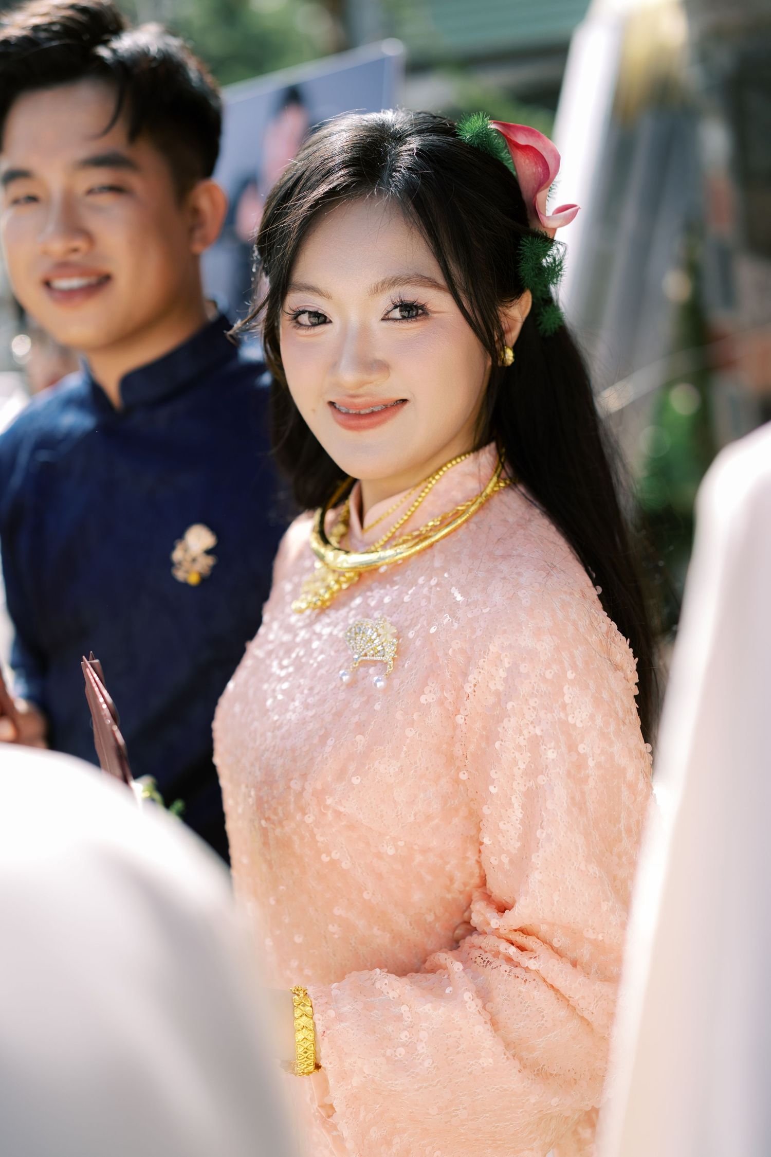 Bride in pink traditional ao dai with gold jewelry and floral hair accessory smiles at wedding.
