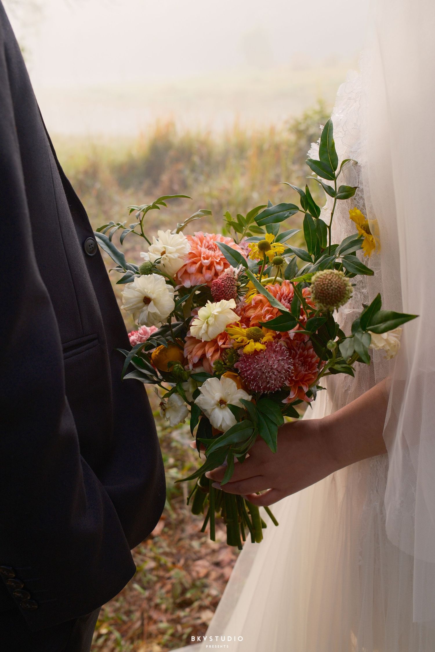 Close-up of bride holding a colorful bouquet of dahlias, white flowers, and greenery on wedding day.