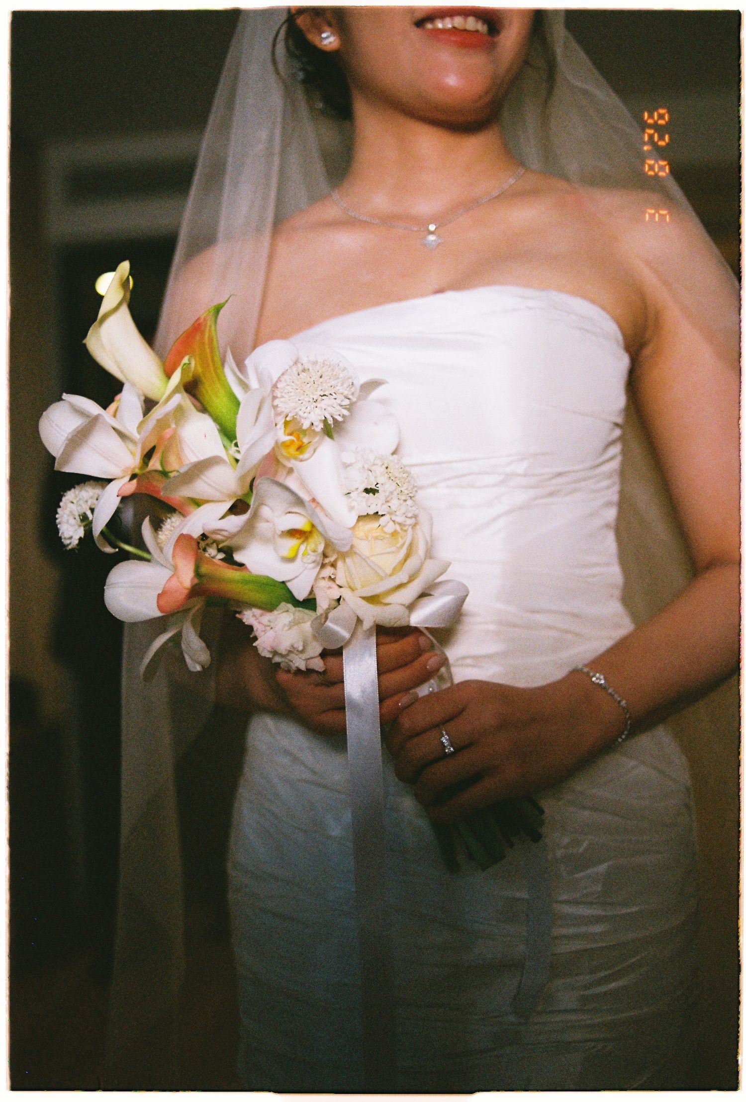Bride in white strapless wedding dress holding elegant white and yellow flower bouquet with ribbon detail.