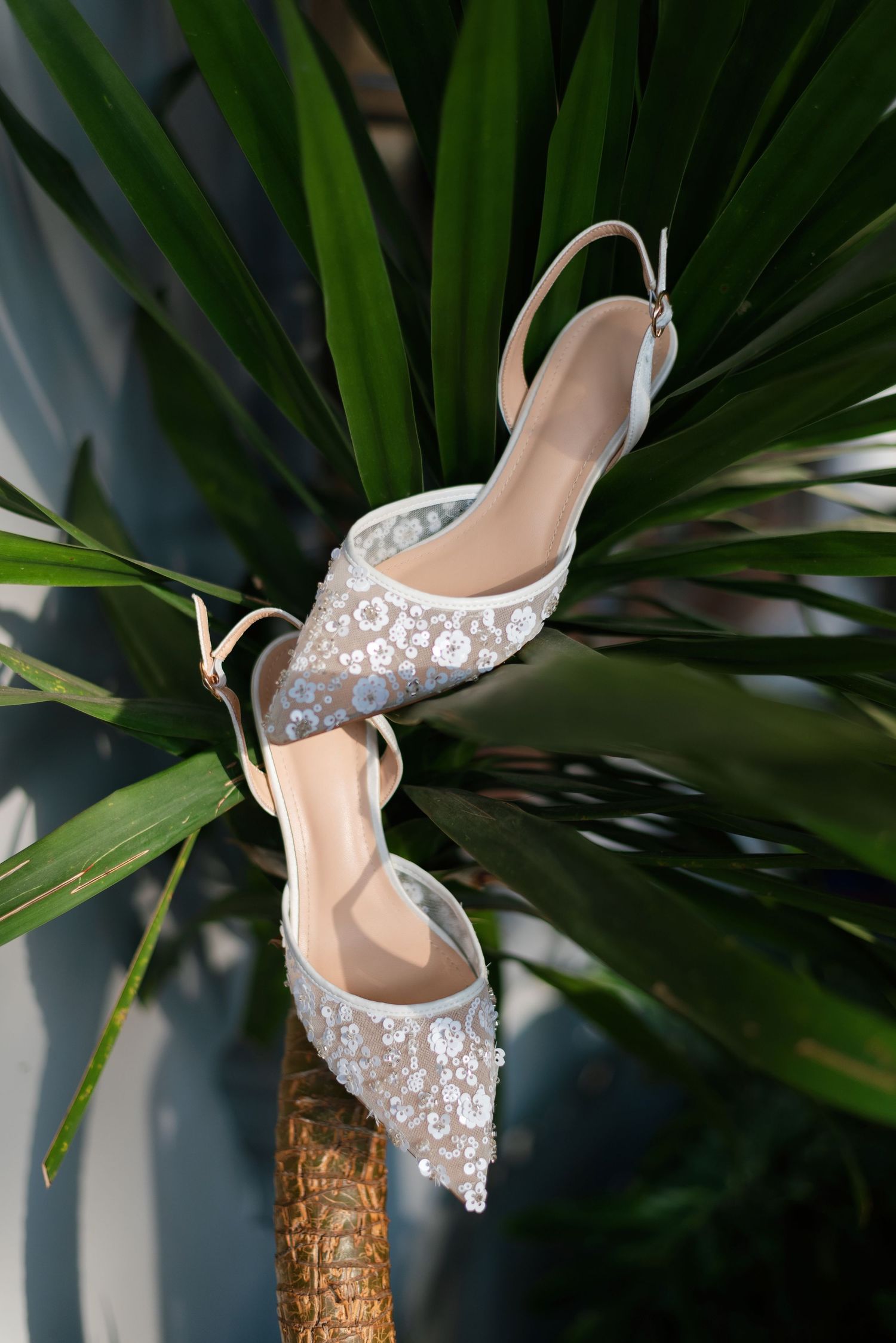 Elegant floral embellished slingback heels displayed on tropical palm plant leaves.