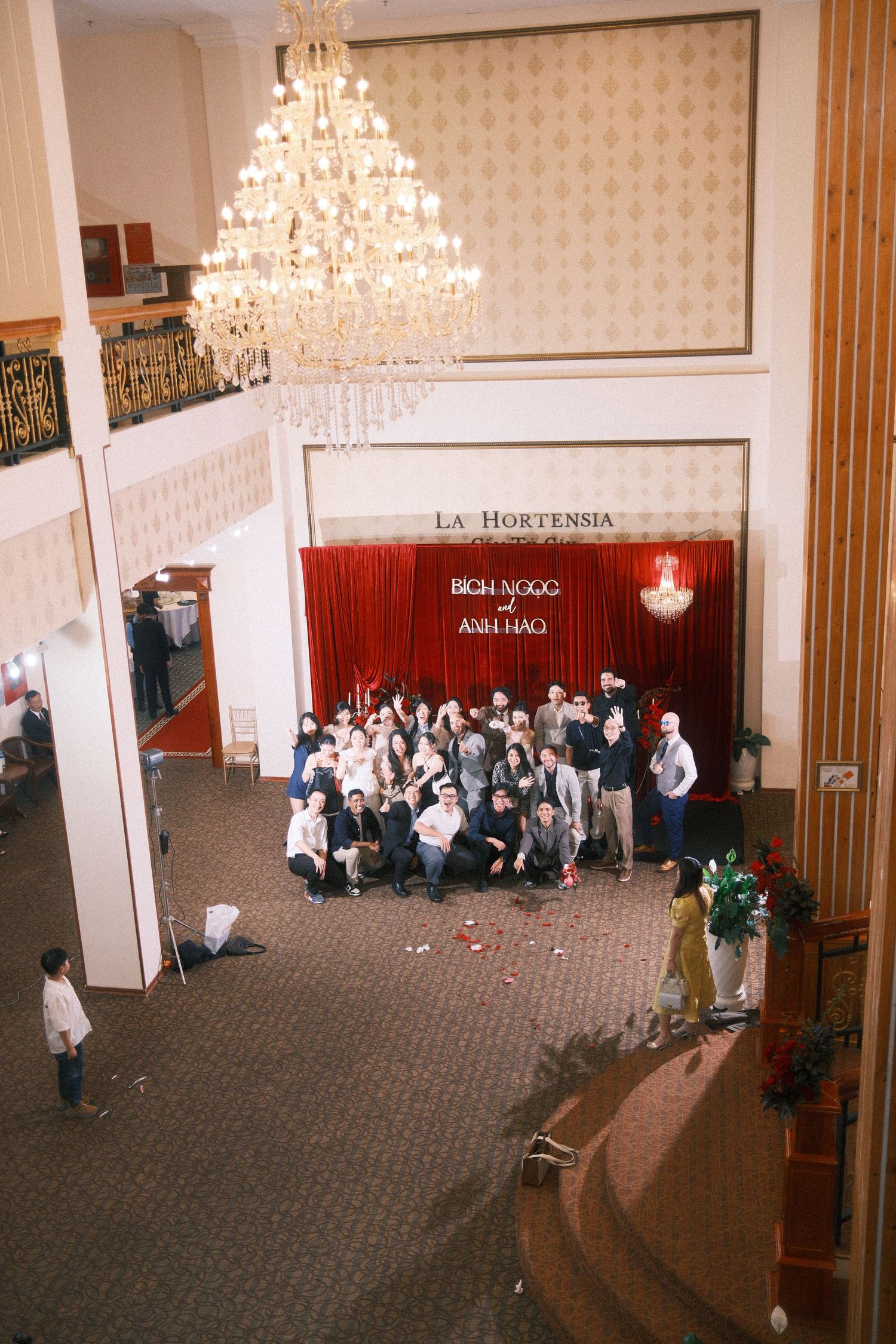 Group photo in La Hortensia hotel lobby with grand chandelier and red backdrop during a formal event.