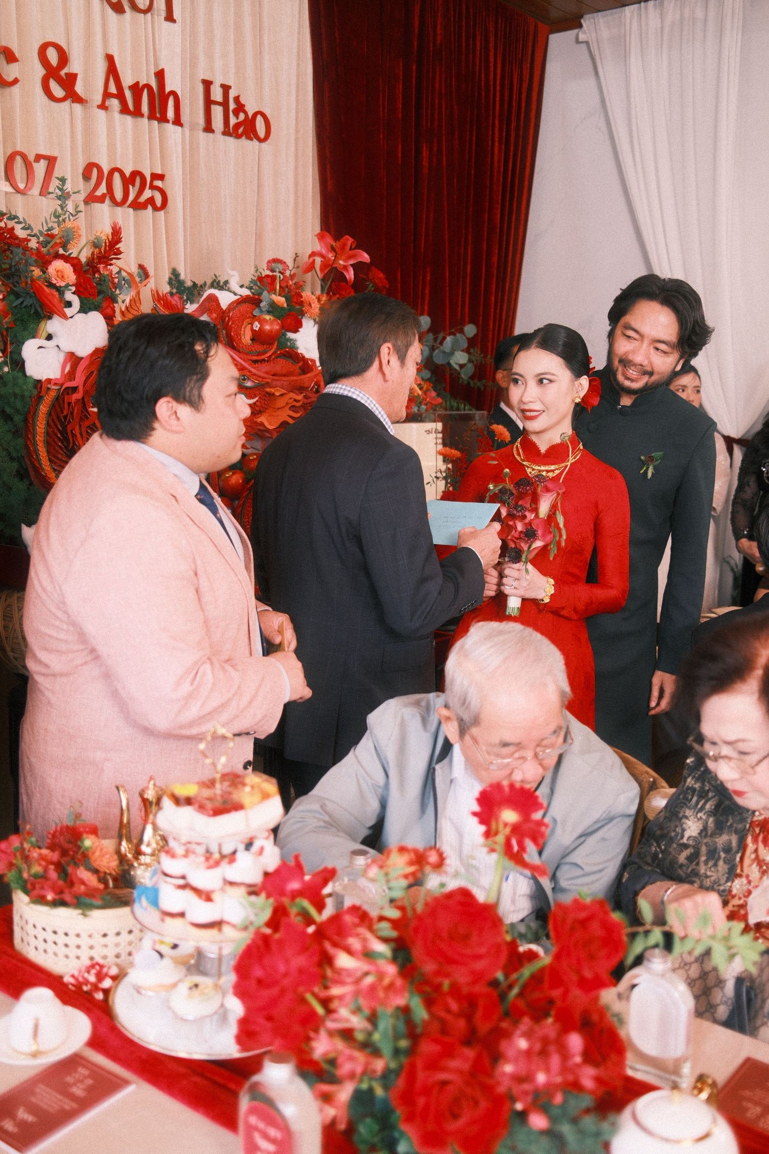 Vietnamese wedding reception with bride in red ao dai receiving guests at decorated table with red roses.