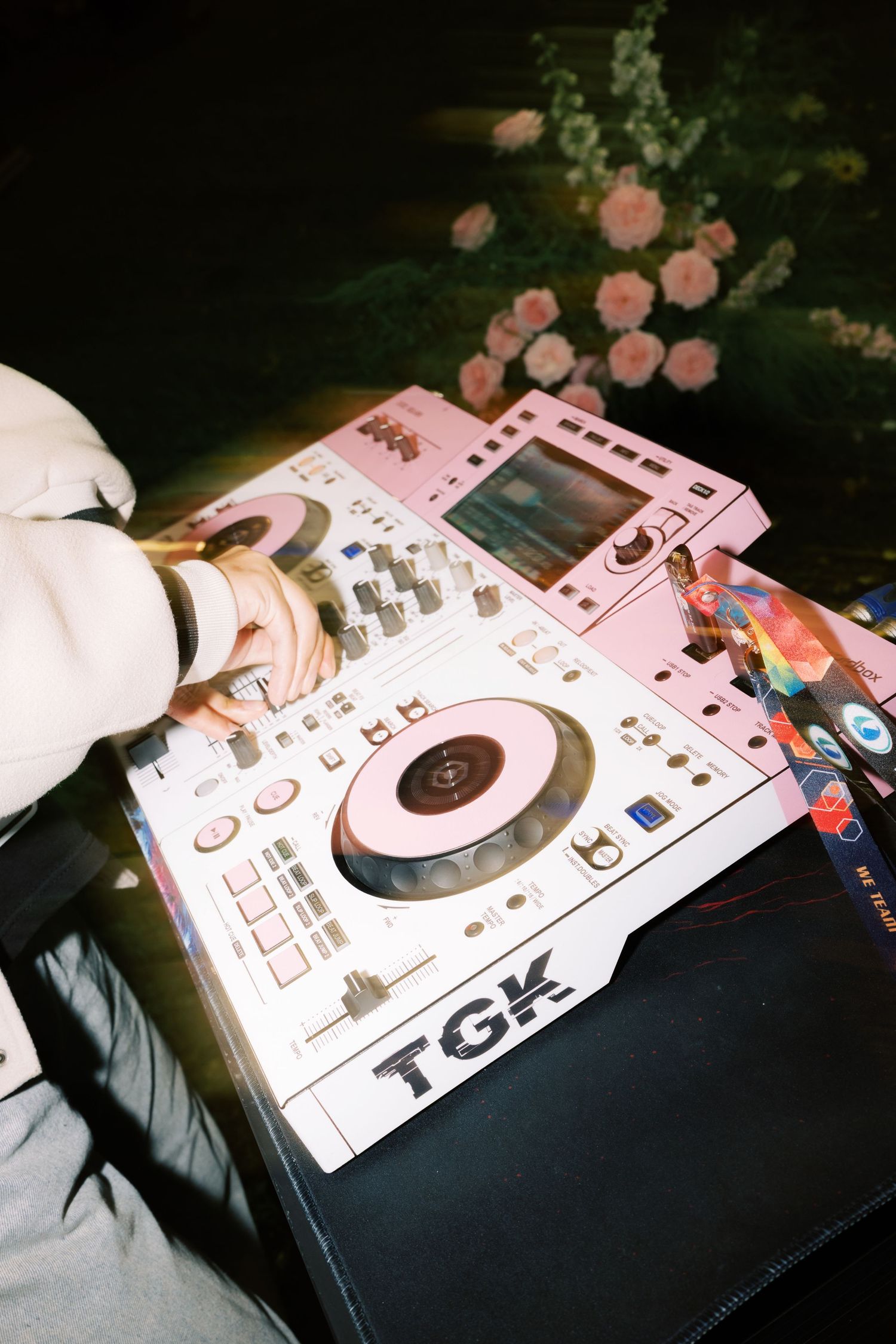 DJ mixing on a pink TGK DJ controller at an event, with pink flowers in the background.