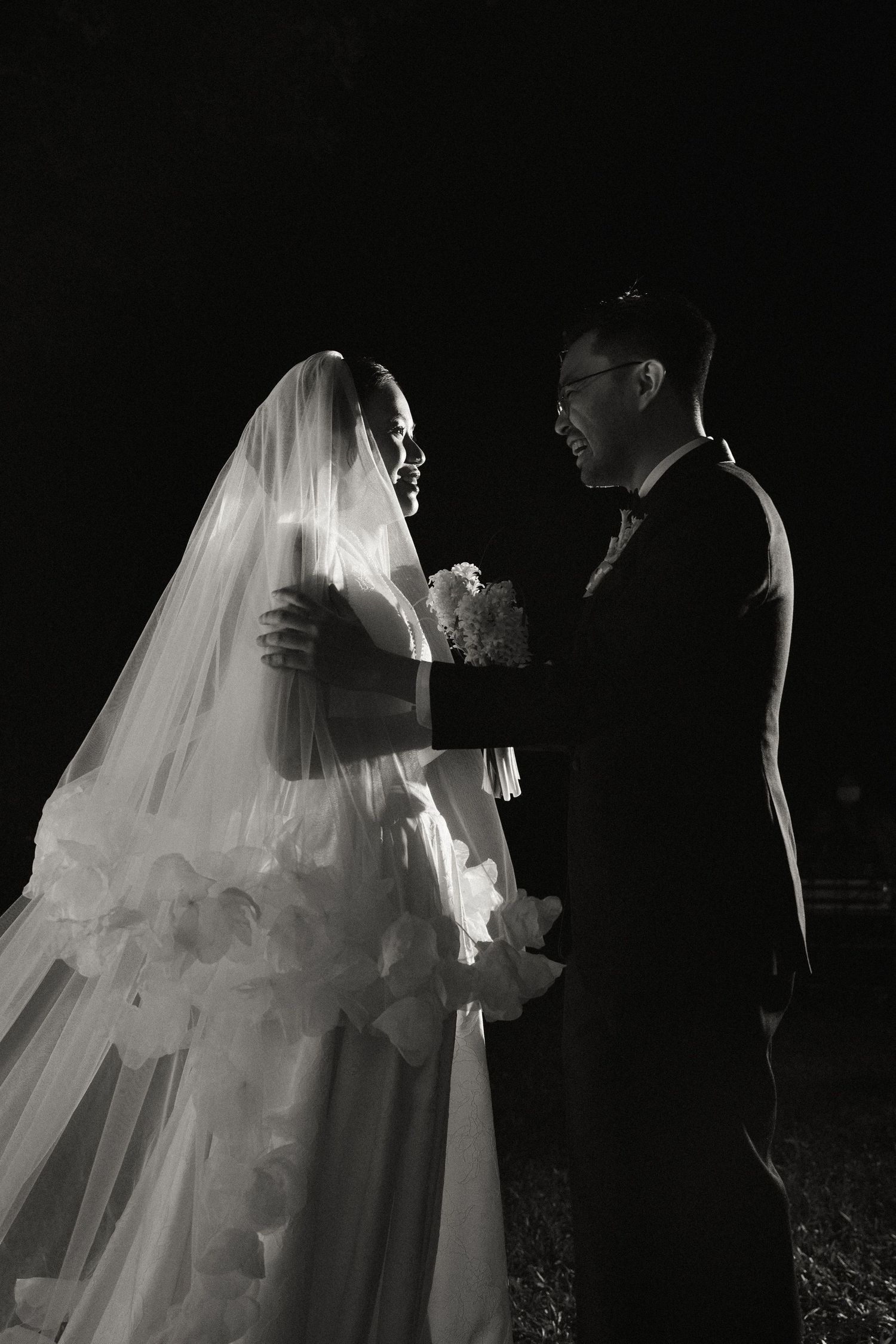Romantic black and white portrait of bride and groom sharing intimate moment at night wedding.