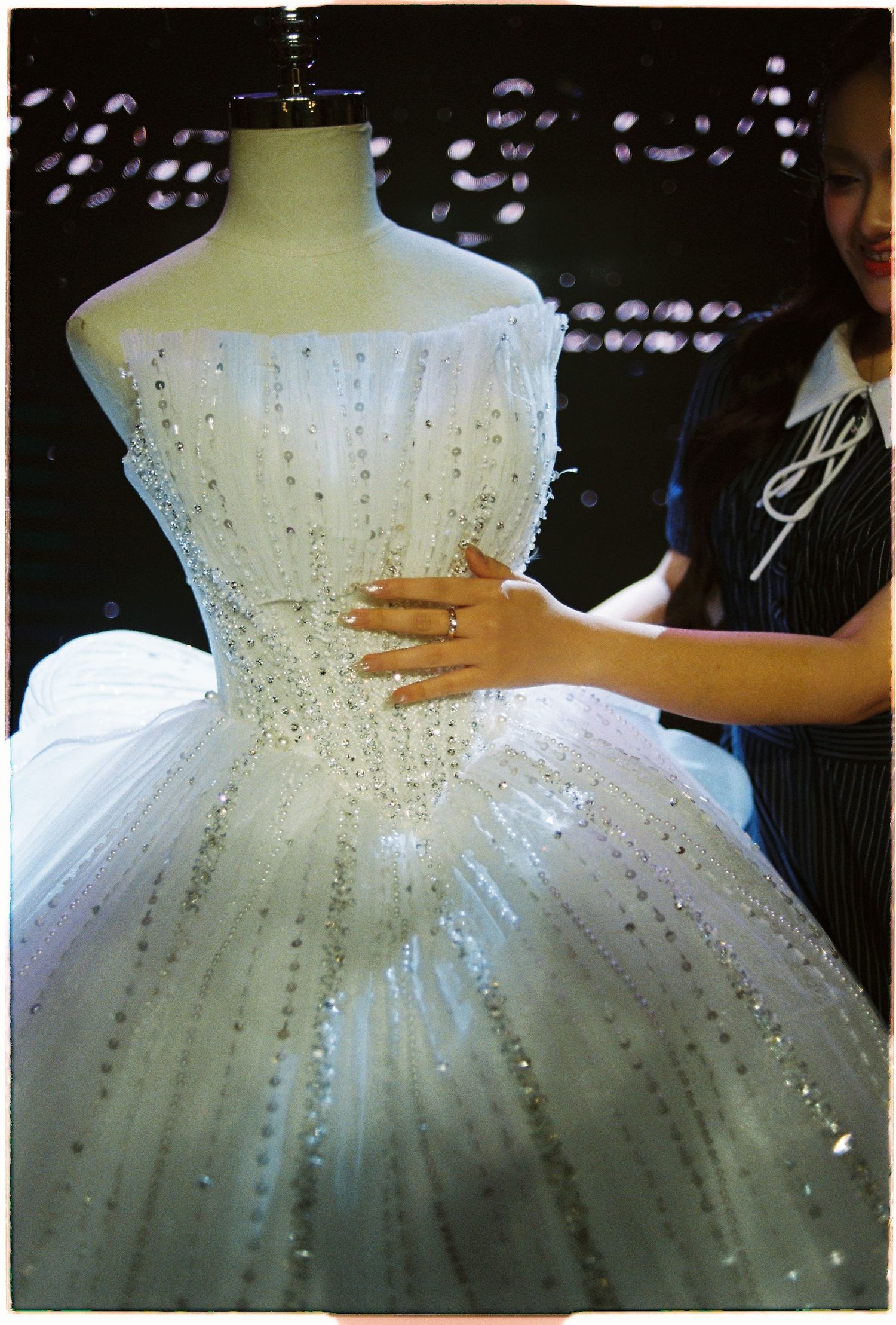 Close-up of a crystal-embellished white wedding ball gown on a mannequin being adjusted by a designer.