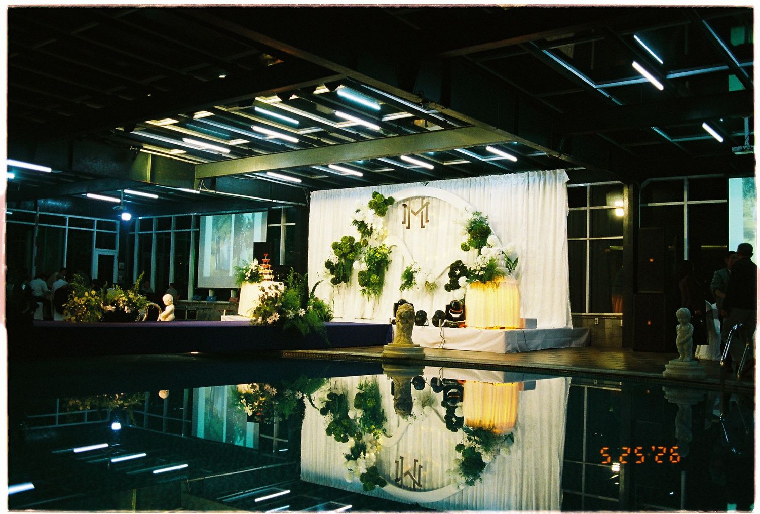 Elegant wedding reception venue with floral stage backdrop reflected in a pool, photographed on 5/25/26.
