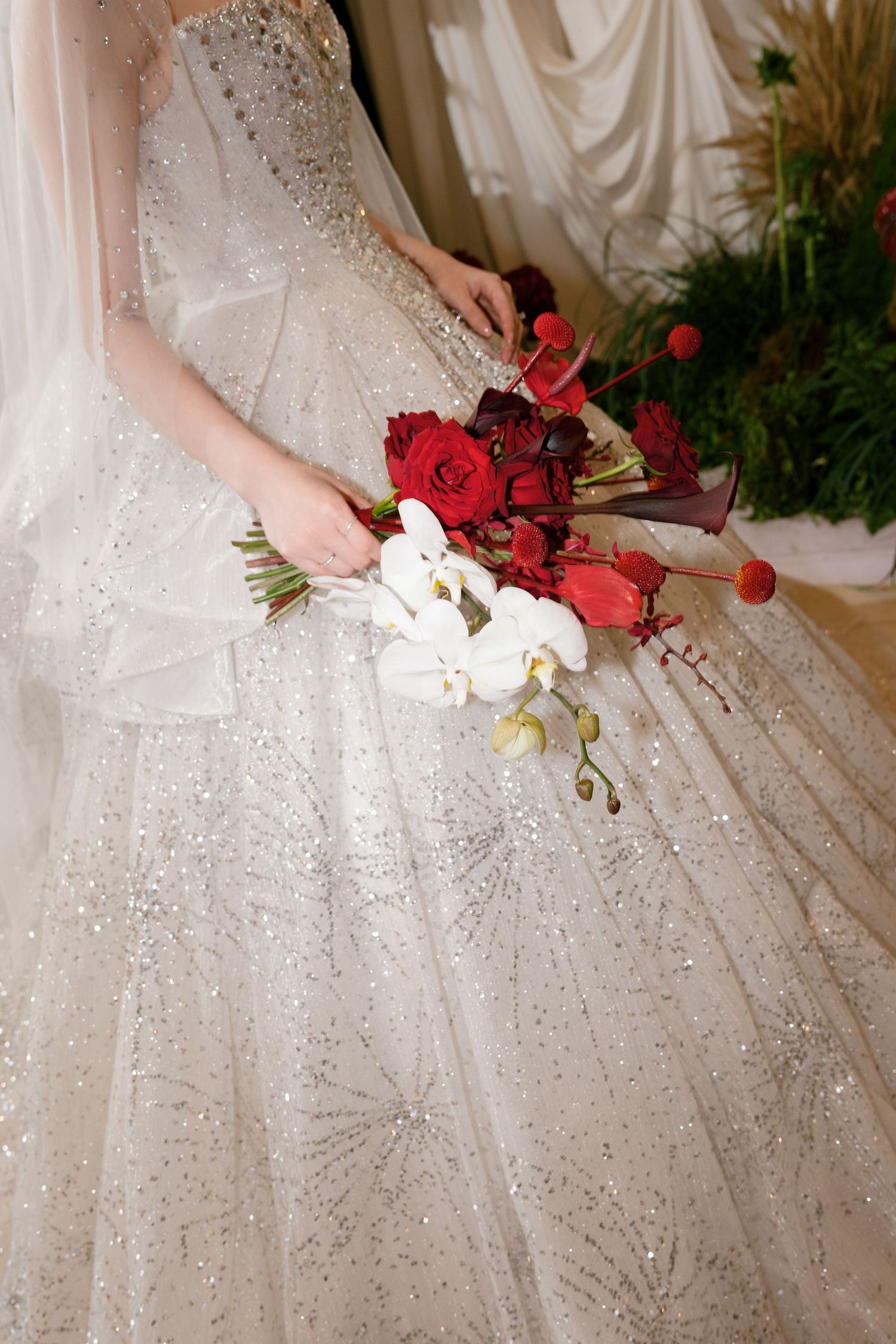 Bride in a sparkling white ballgown holding a bridal bouquet of red roses and white orchids.
