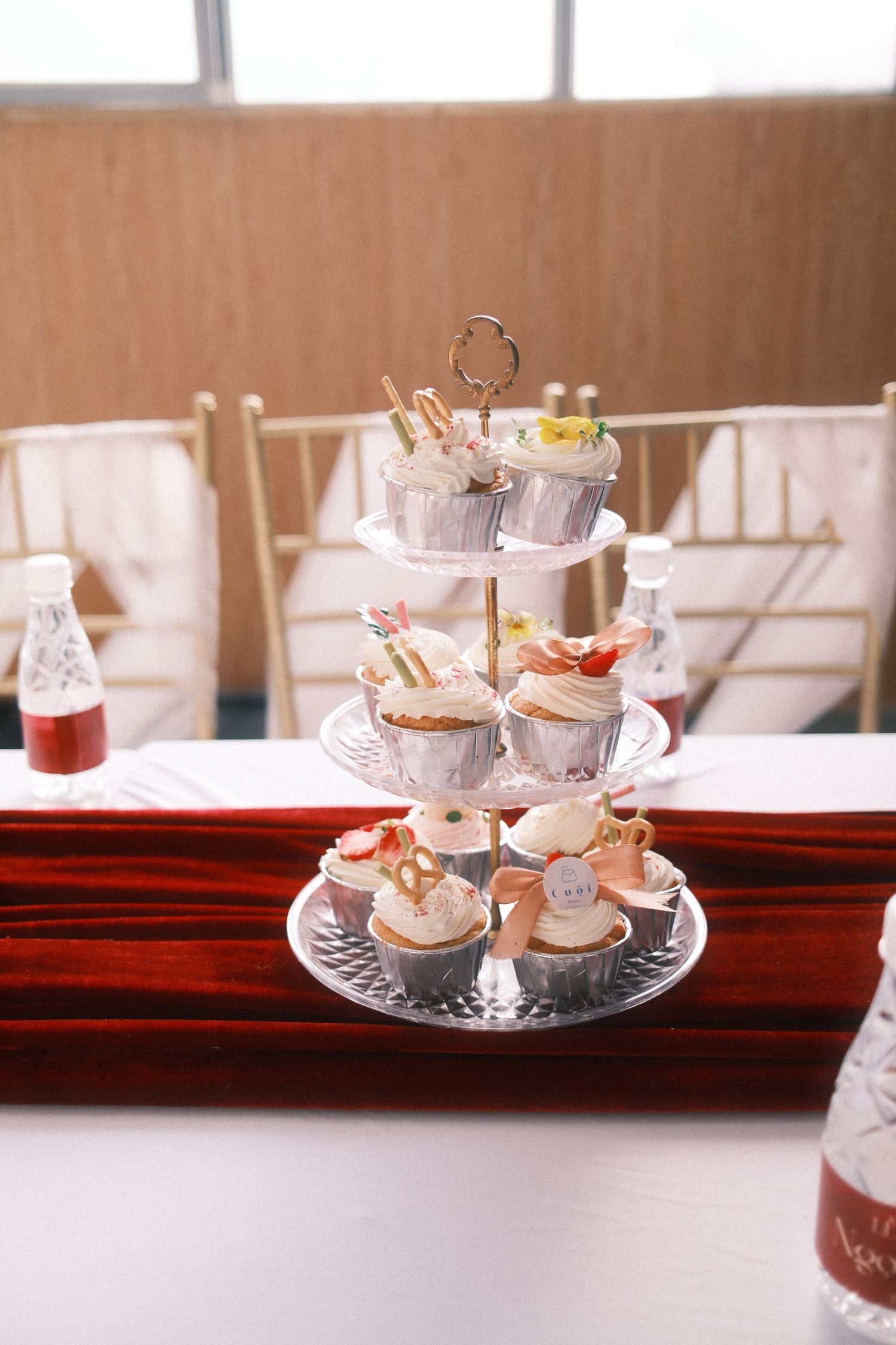 Three-tier cupcake stand displaying decorated cupcakes at an elegant event with red satin table runner.