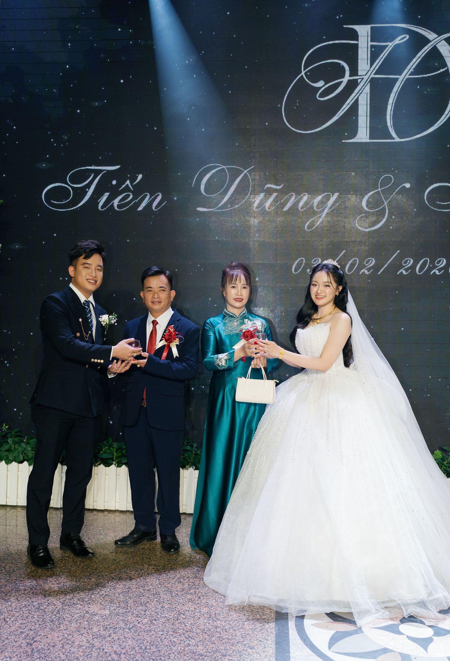 Wedding couple with family posing at Vietnamese reception with elegant backdrop.