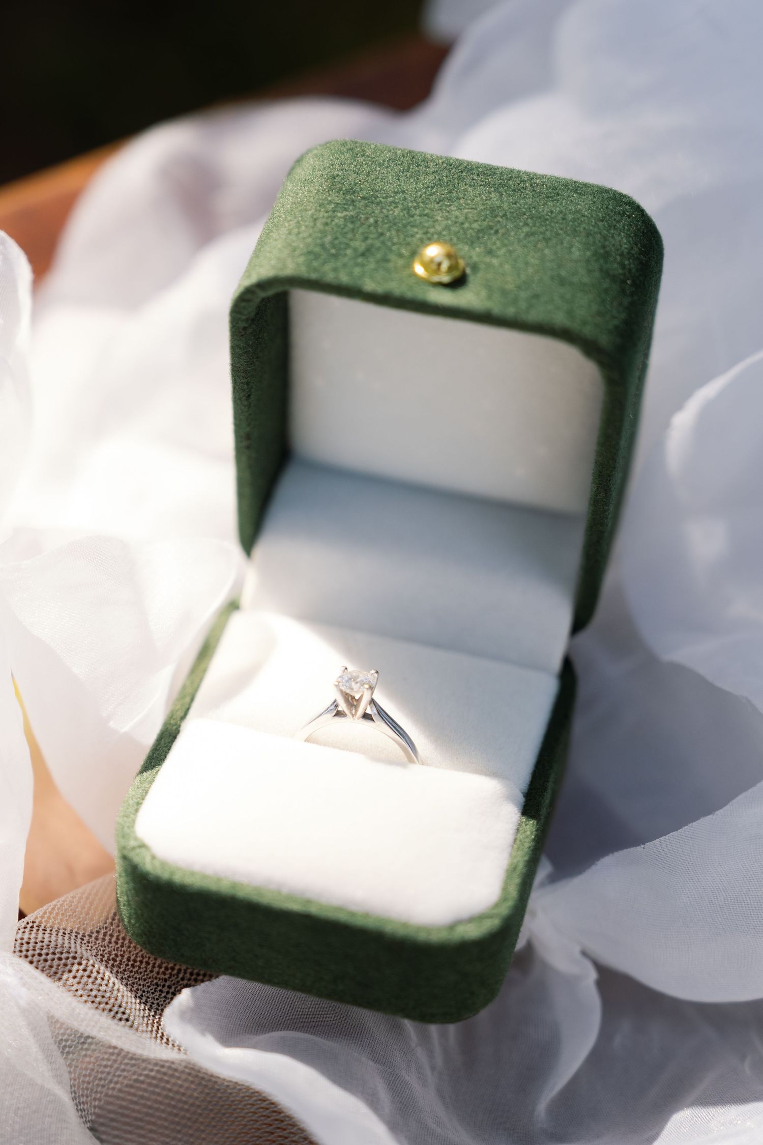 Diamond solitaire engagement ring displayed in an open green velvet jewelry box.