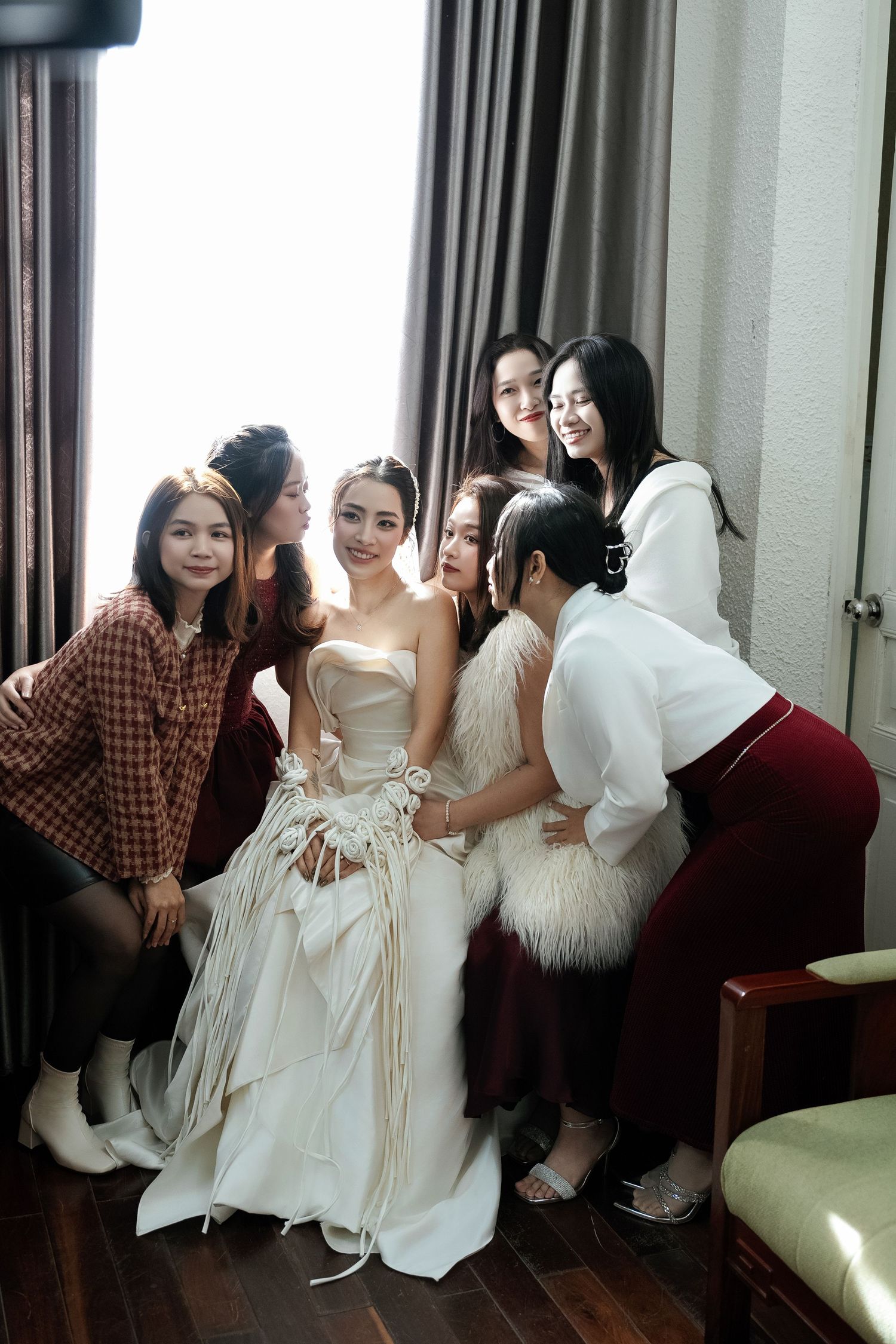 Bride in white wedding gown surrounded by bridesmaids in hotel room.