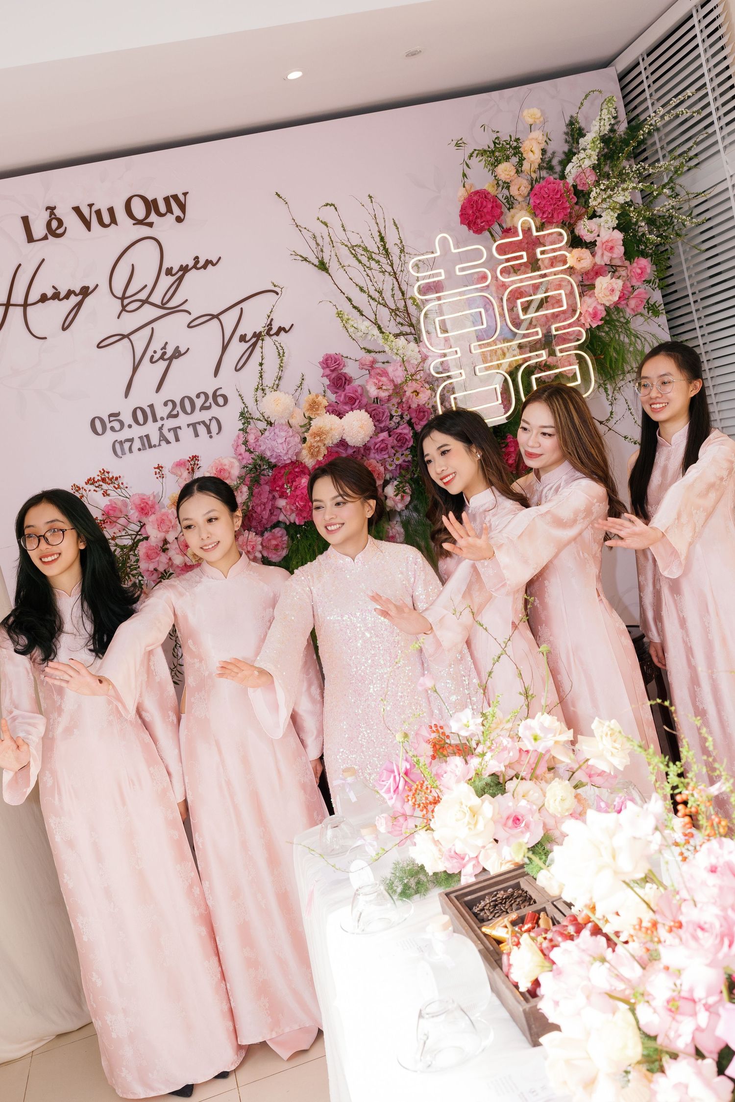 A bride in a pink sequined ao dai poses with bridesmaids in matching pink ao dai at a Vietnamese wedding.
