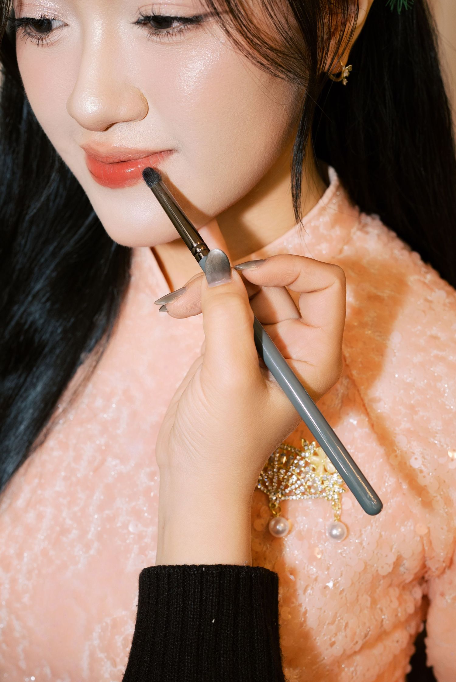 A makeup artist applies lipstick to a young Asian woman wearing a pink sequined ao dai dress.