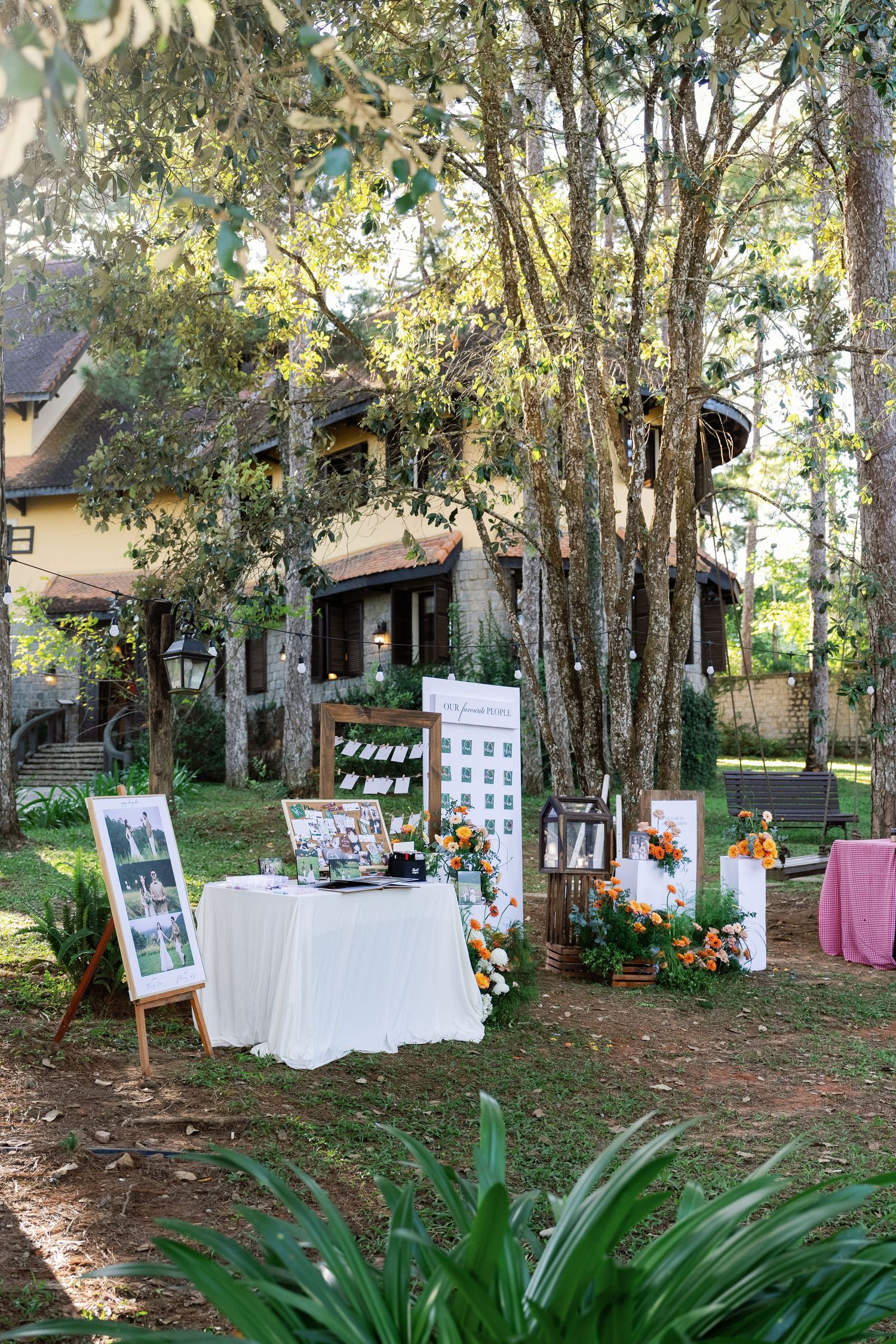 Outdoor wedding reception welcome table with floral arrangements, seating chart, and rustic decor in garden setting.