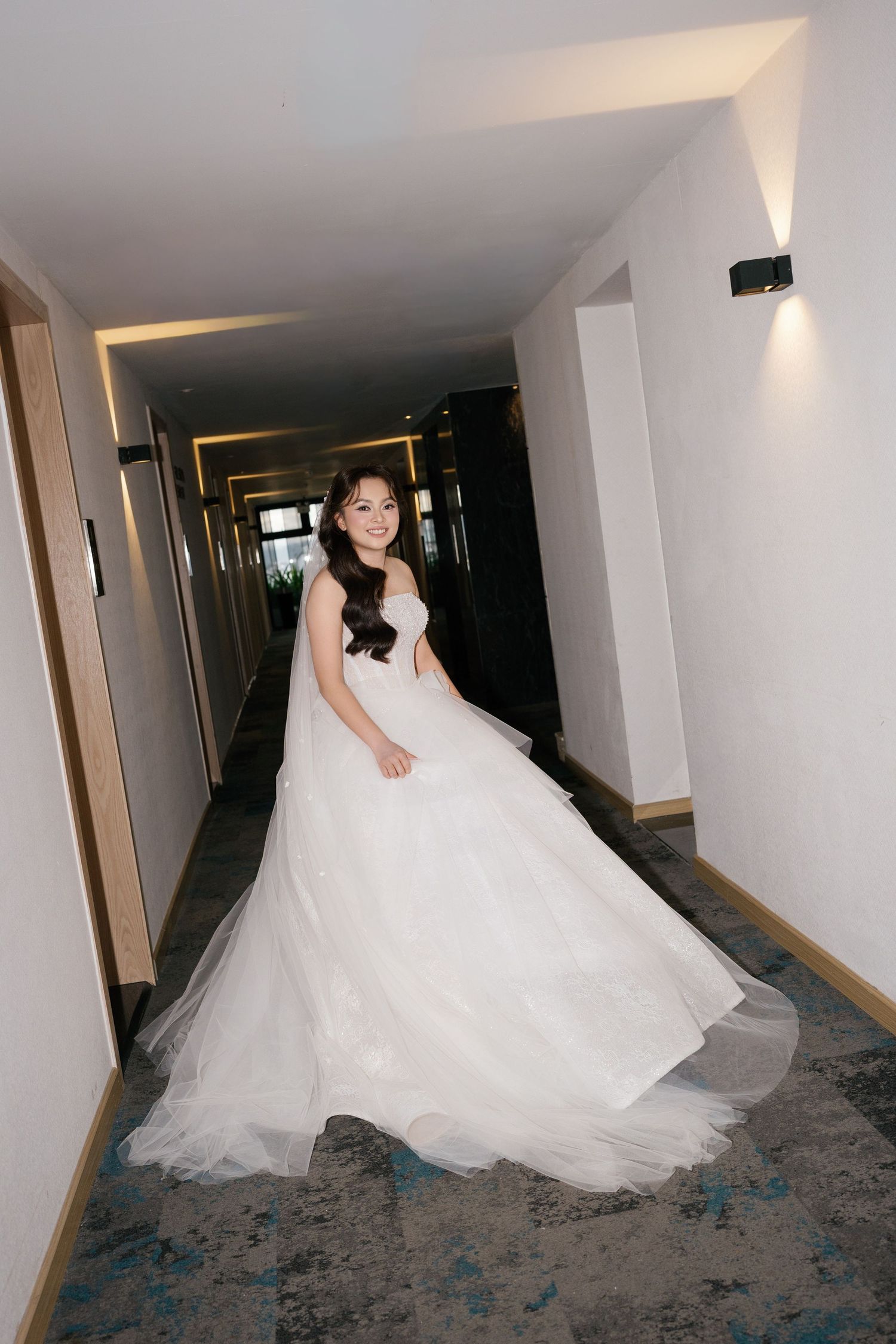 Bride in a flowing white ballgown twirling in a hotel corridor, smiling radiantly on her wedding day.