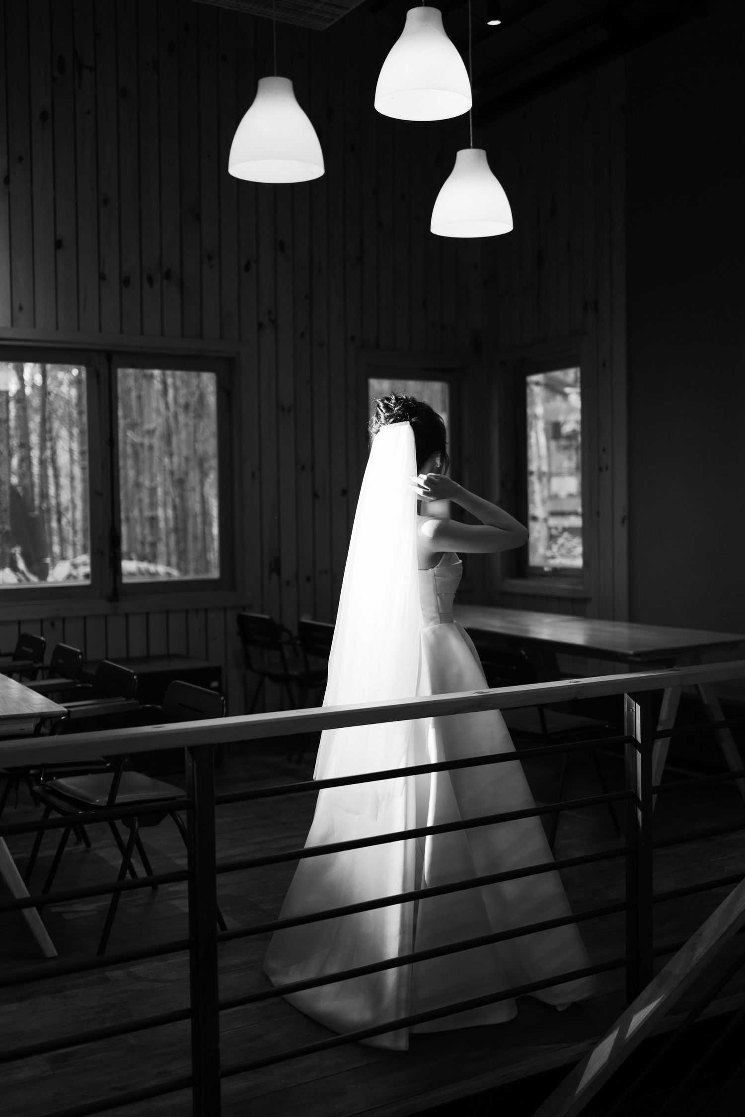 Bride in white gown and veil stands on balcony in black and white wedding photo.