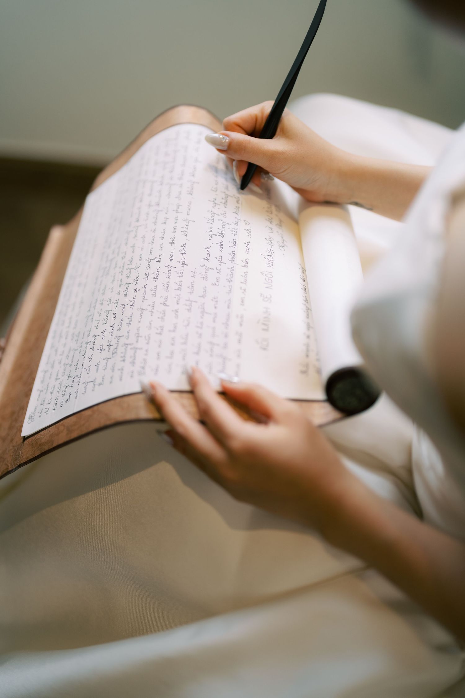 Close-up of hands writing elegant cursive script in an open book using a black calligraphy pen.