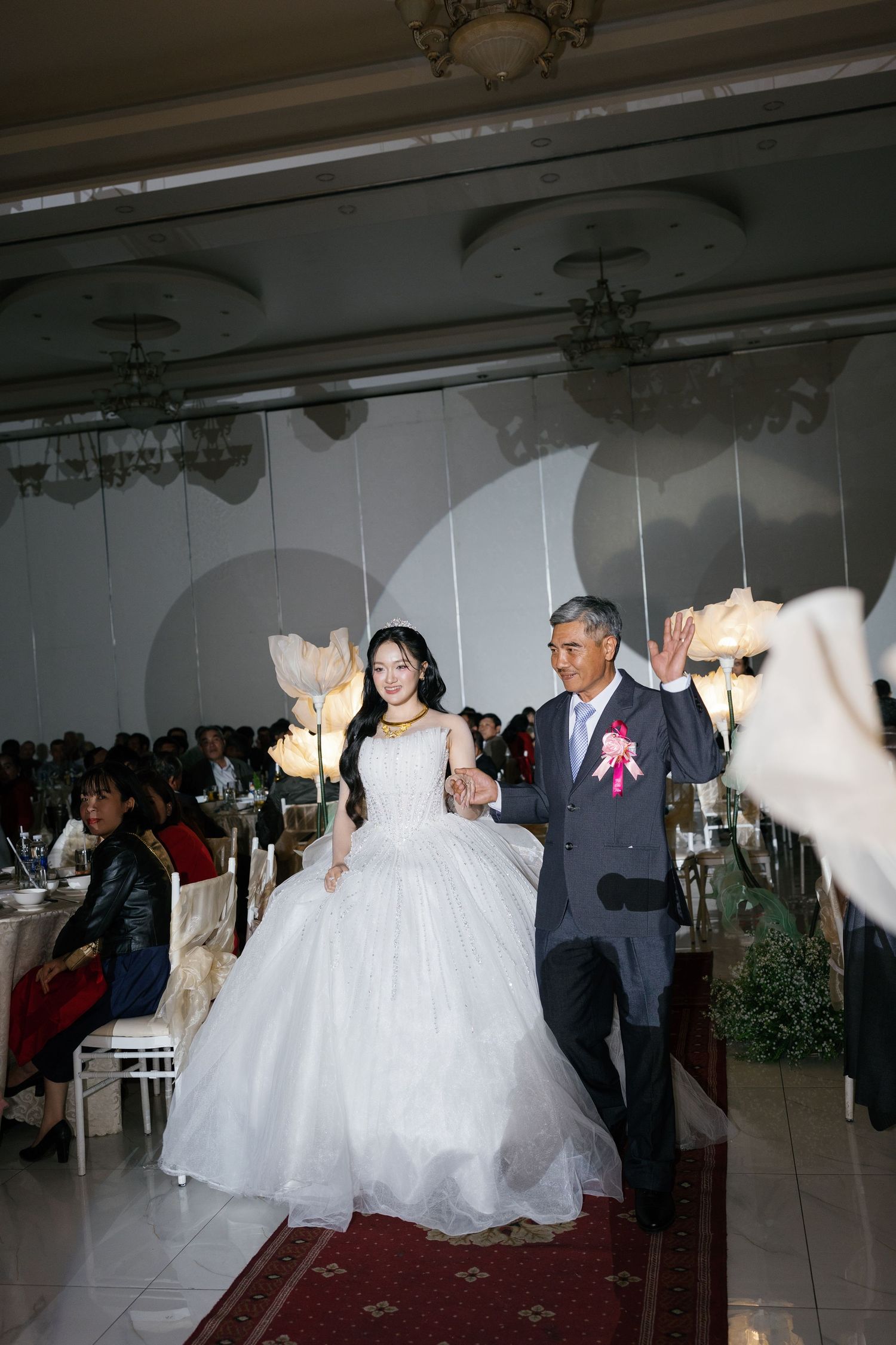 Bride in white ball gown walks down the aisle with her father at wedding reception.