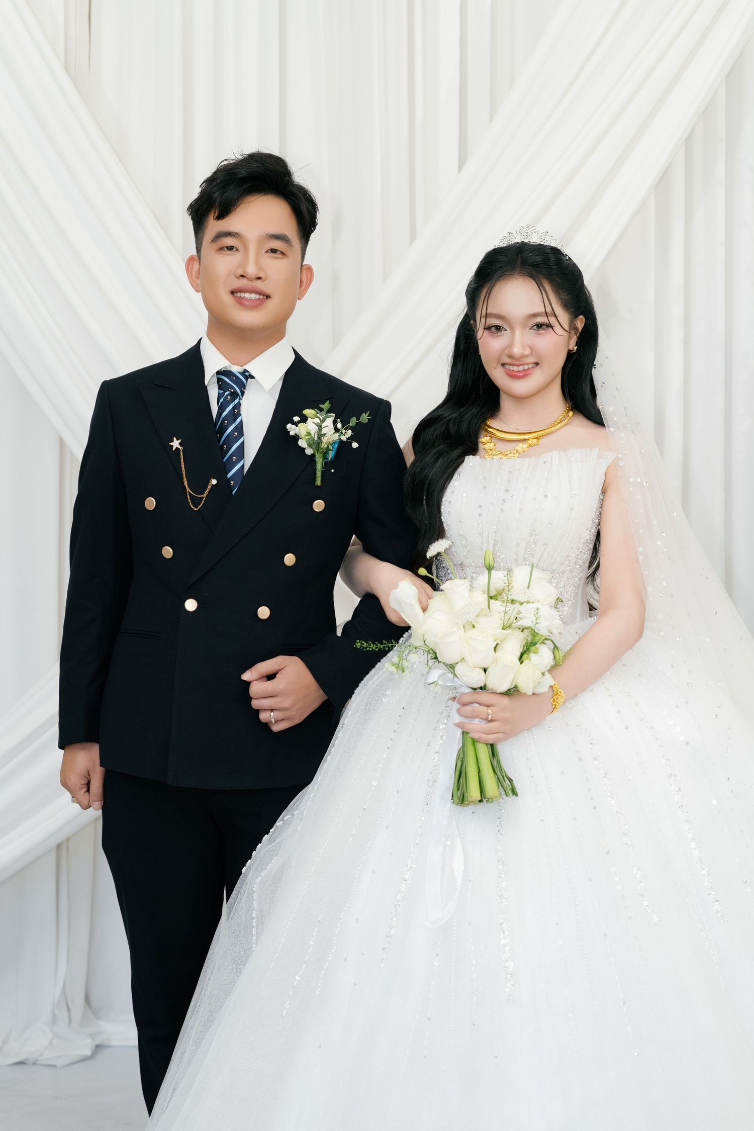 Vietnamese wedding couple posing together, groom in black suit and bride in white ball gown holding bouquet.