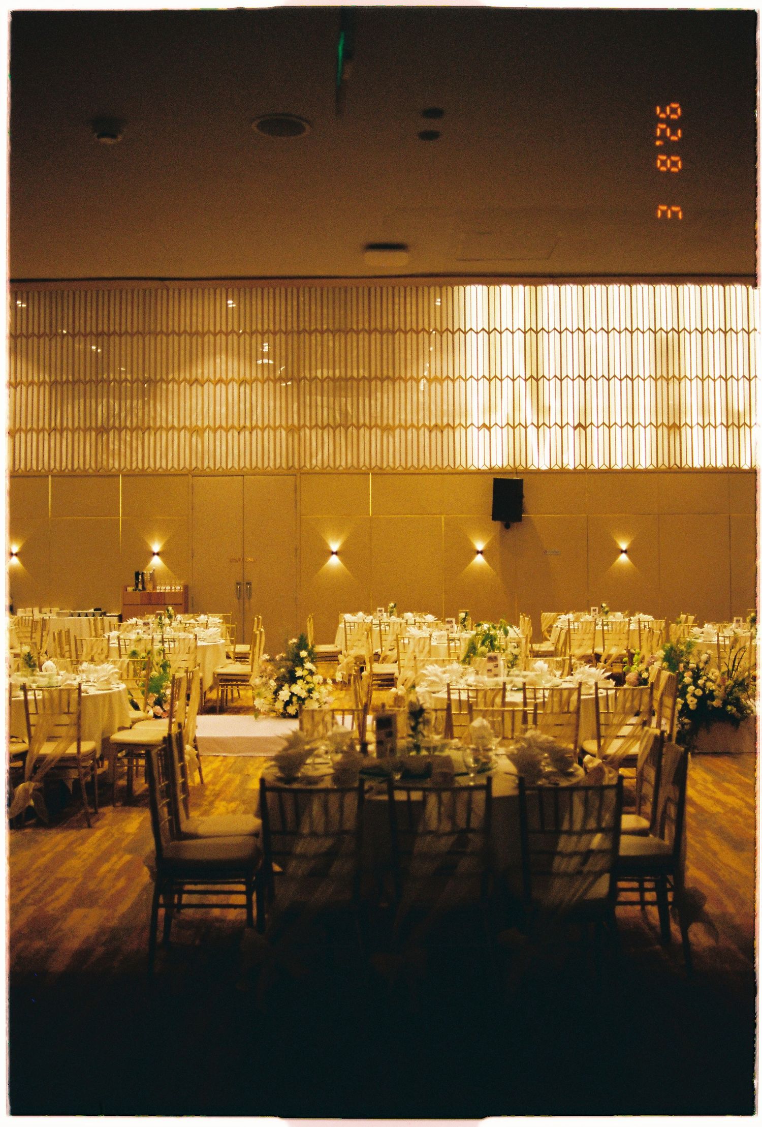 Elegant wedding reception hall with round tables, gold chiavari chairs, floral centerpieces, and warm ambient lighting.