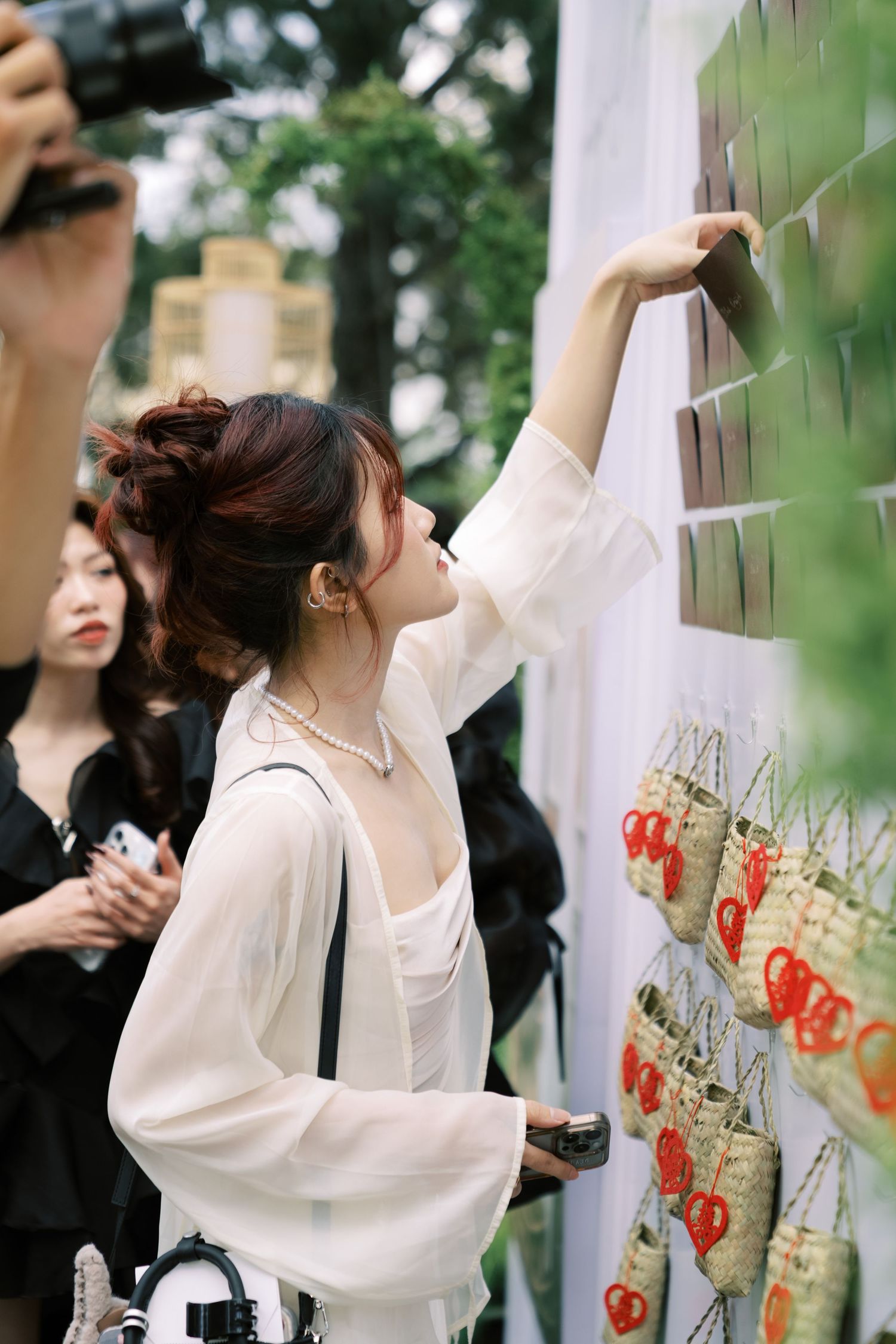 A woman in white reaches up to a seating chart wall adorned with woven basket favors at an outdoor wedding reception.