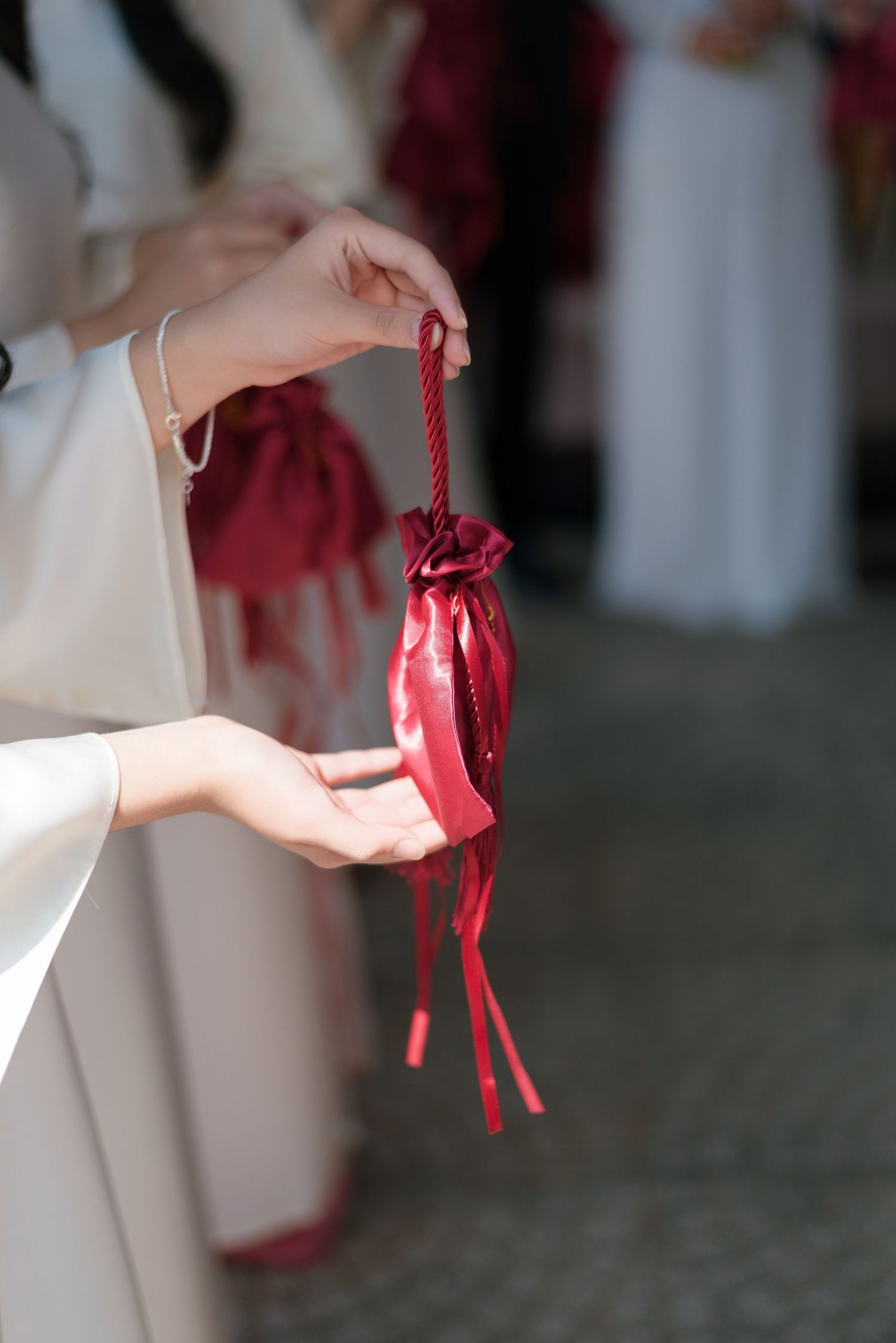 Hands holding a red satin drawstring gift bag with decorative ribbons at a traditional ceremony.