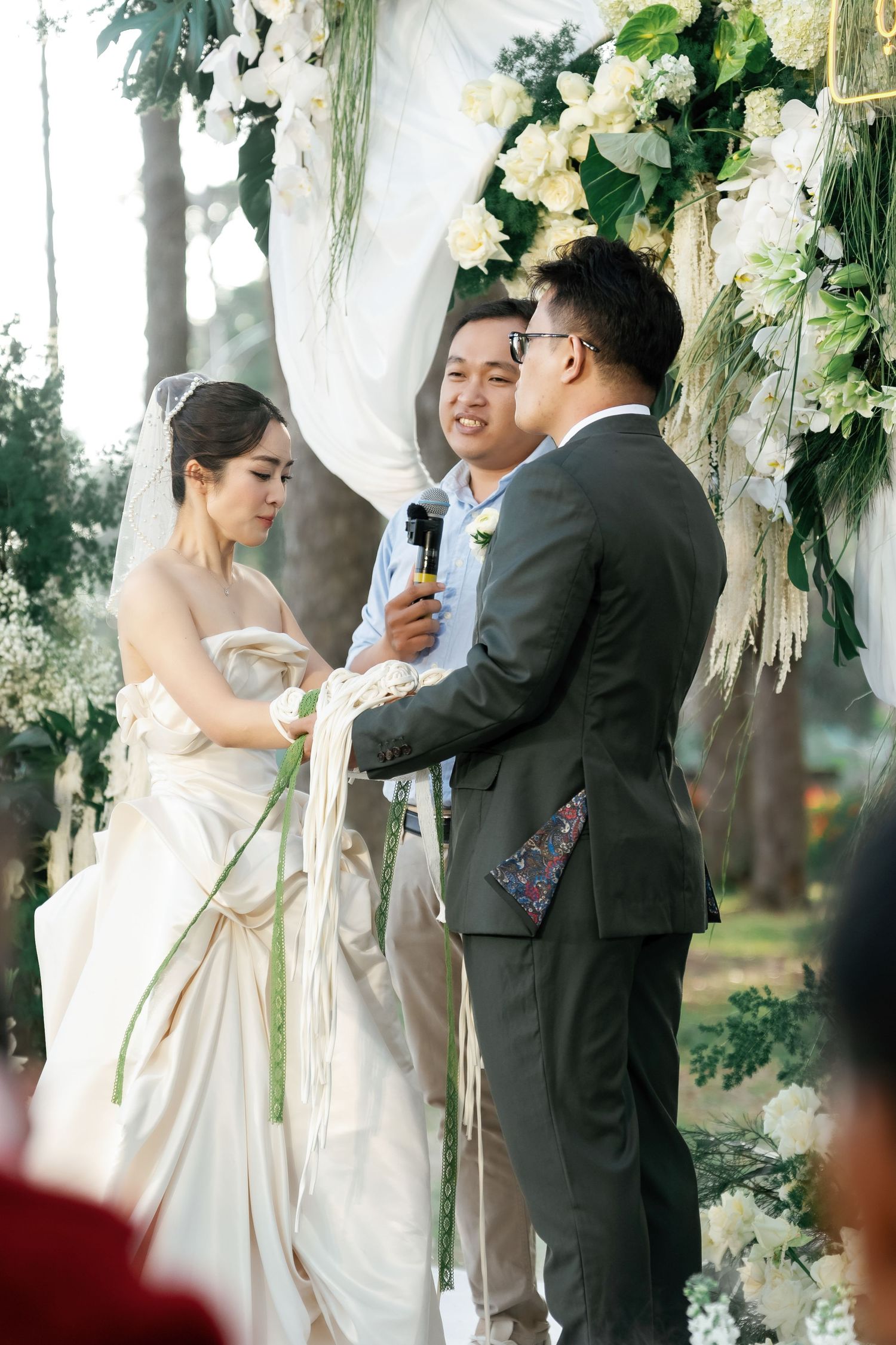 Bride and groom exchanging vows at outdoor wedding ceremony beneath floral arch with officiant.