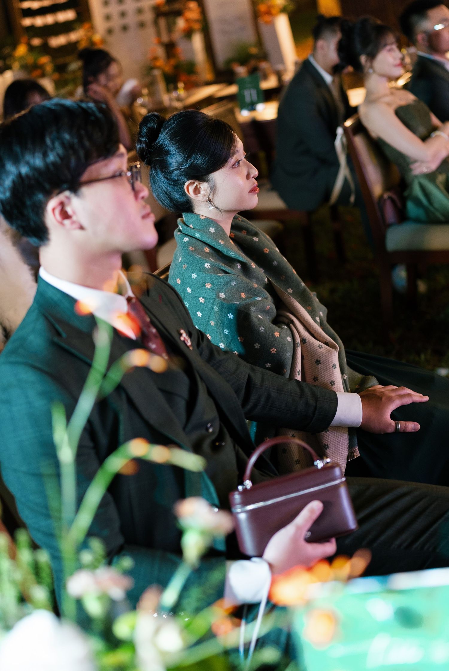 Wedding guests in formal attire seated at decorated reception tables during evening celebration.