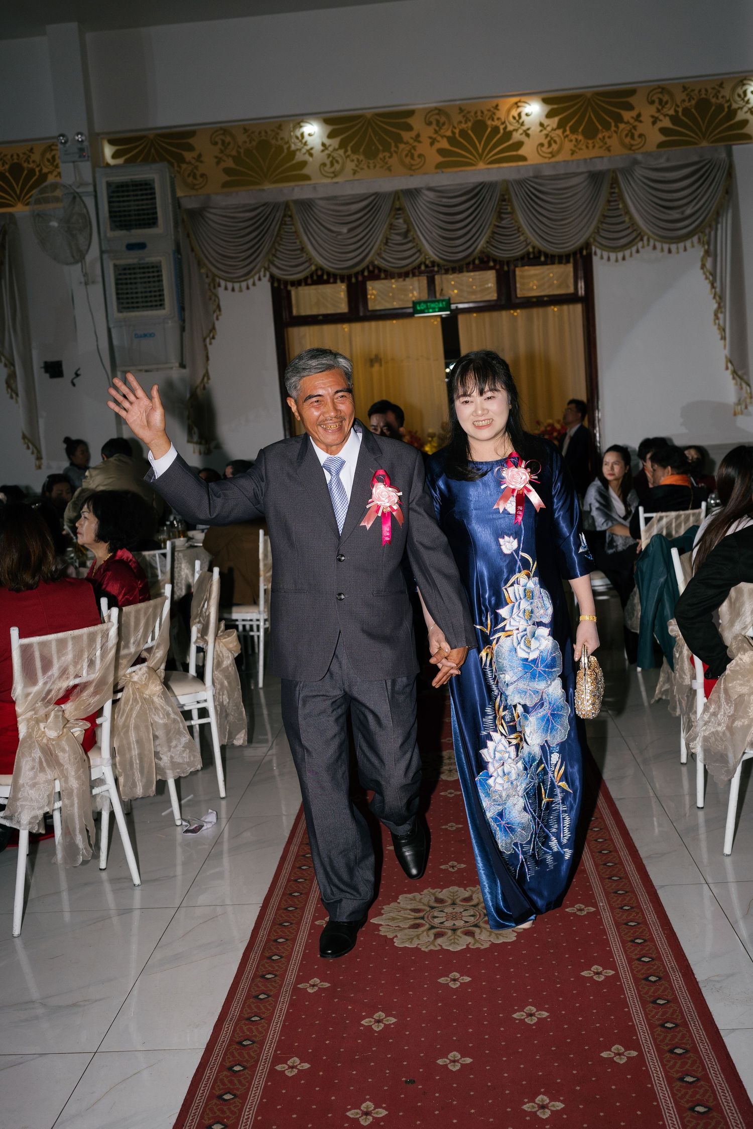 Elegant couple in formal attire walk down red carpet aisle at wedding celebration.