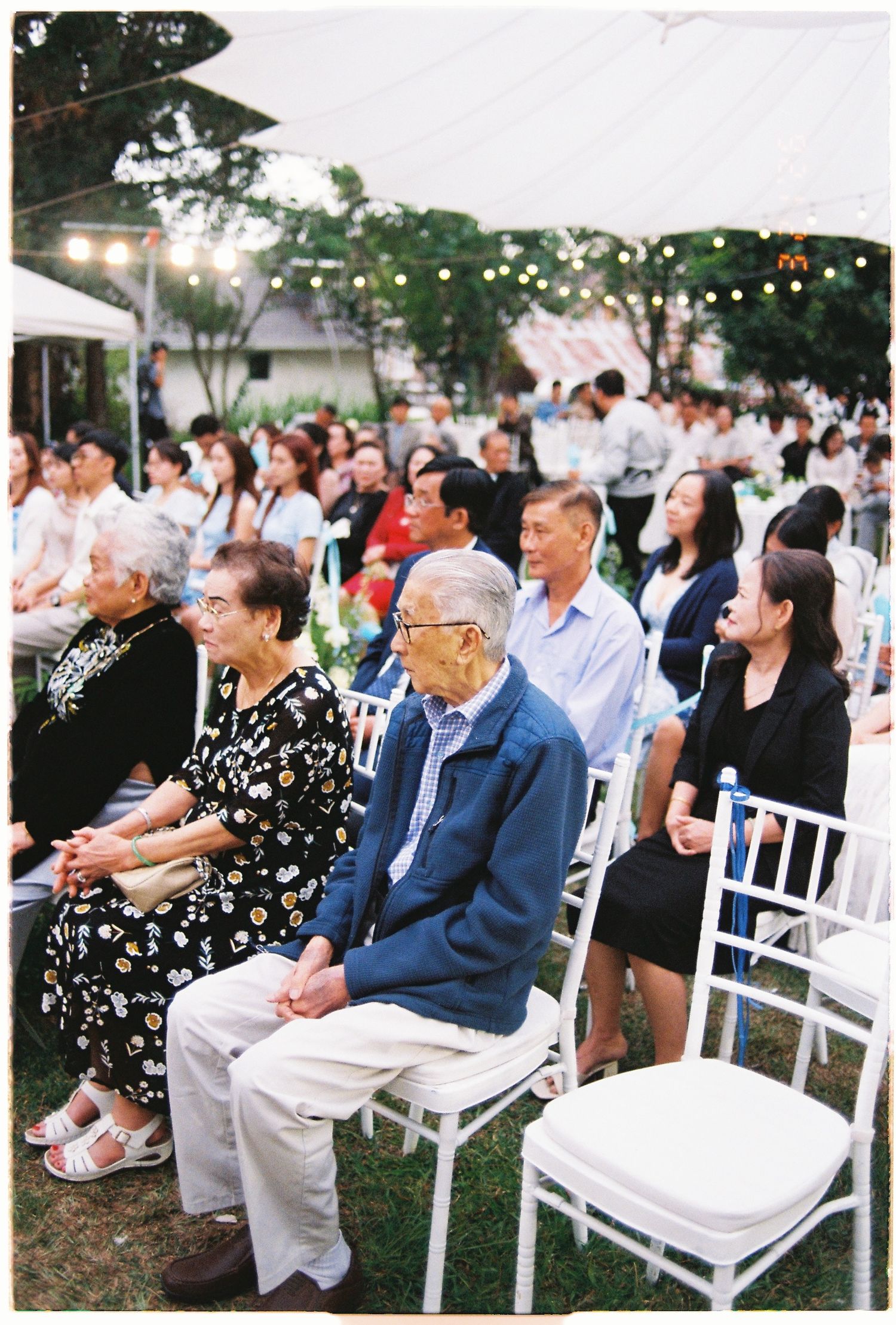 Guests seated on white chairs at an outdoor evening event under string lights.