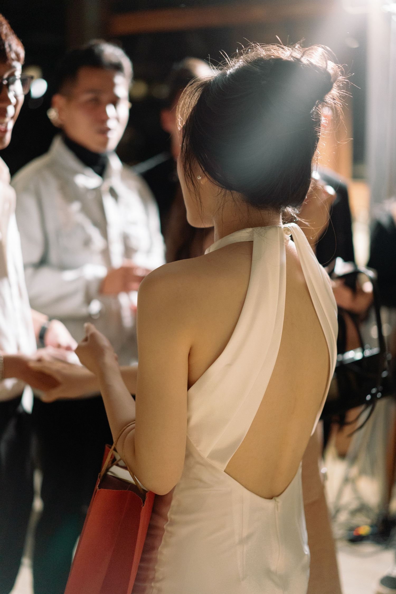 Back view of Asian woman in cream halter dress with updo hairstyle at evening wedding event.