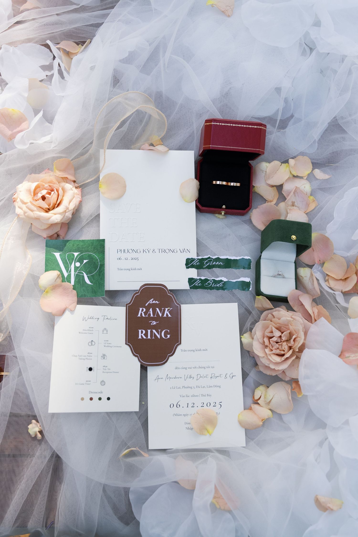 Flat lay of elegant wedding stationery suite with rings, roses, and petals on tulle fabric.