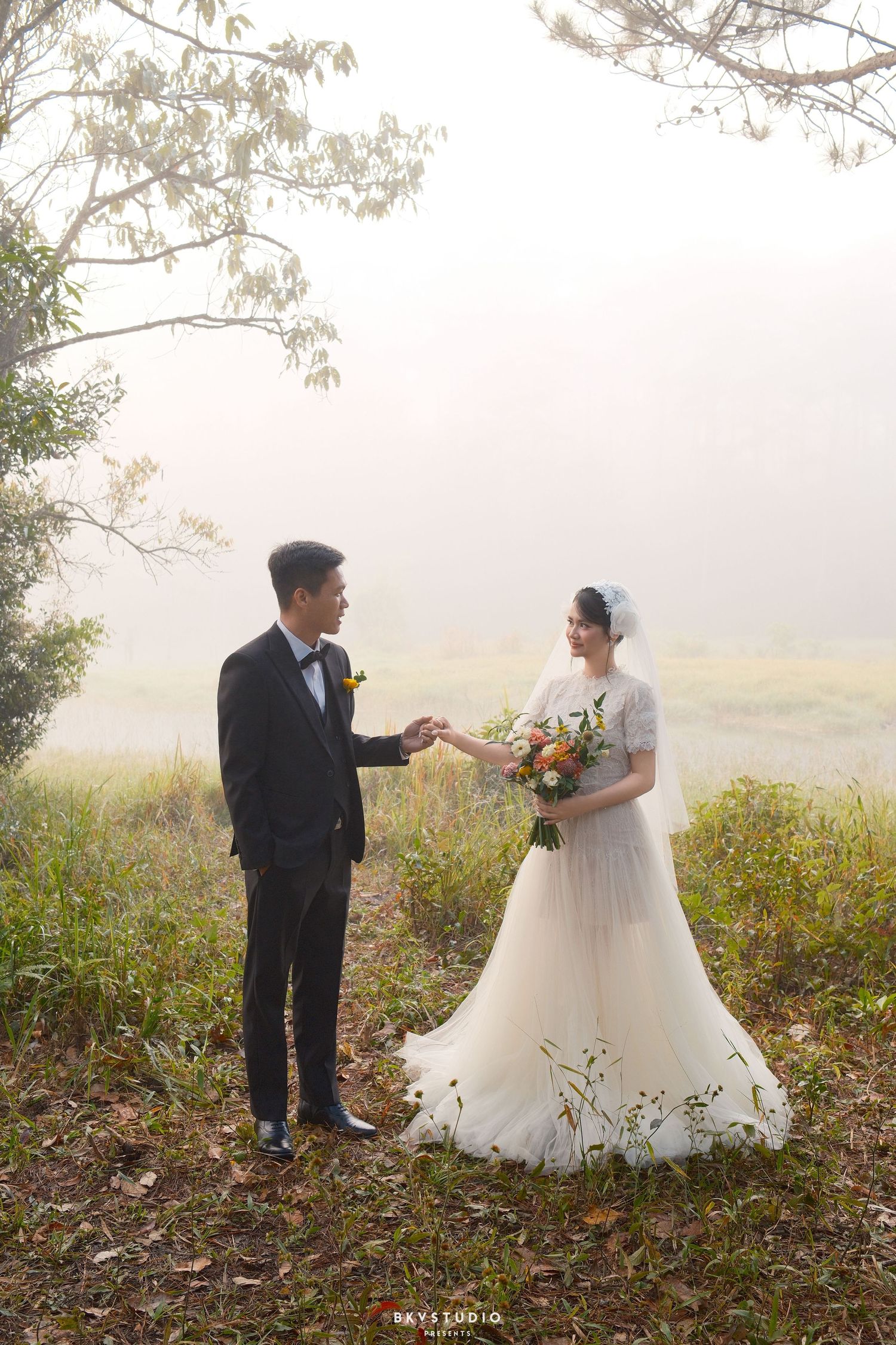 Bride and groom exchange rings in a romantic misty outdoor setting during their wedding photo session.