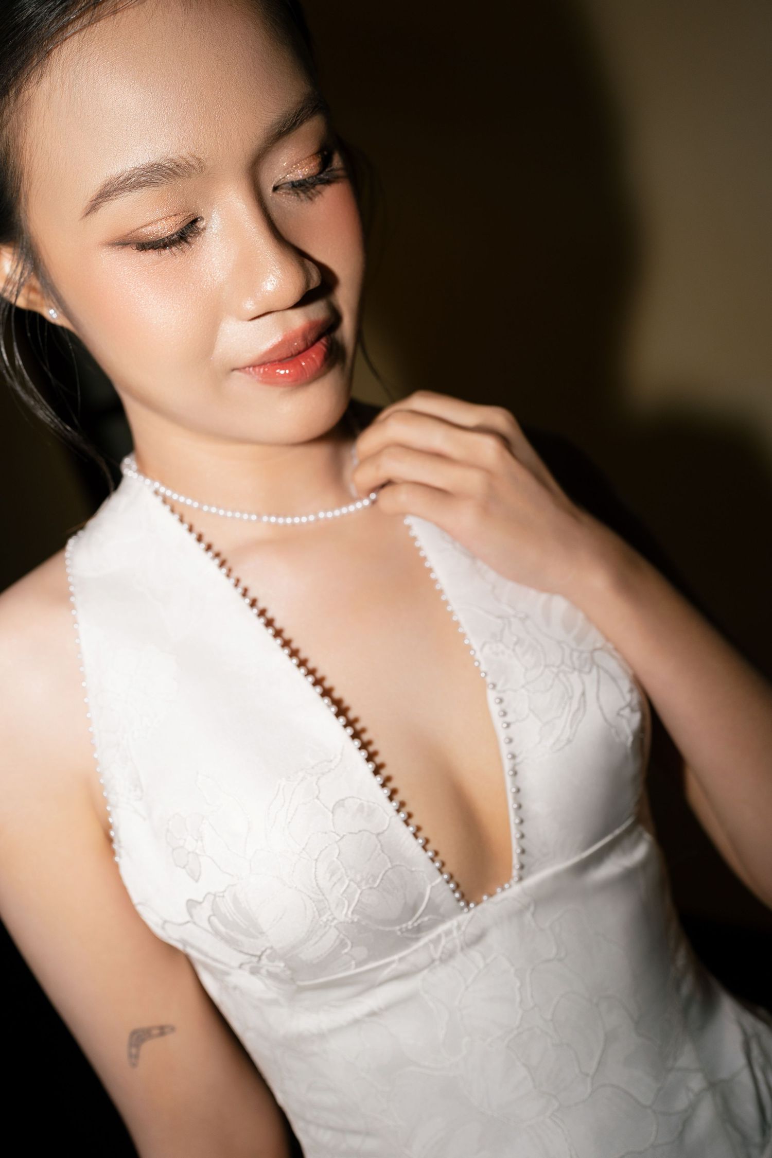 Close-up of bride in deep V-neck lace wedding dress with long pearl necklace looking down gracefully.