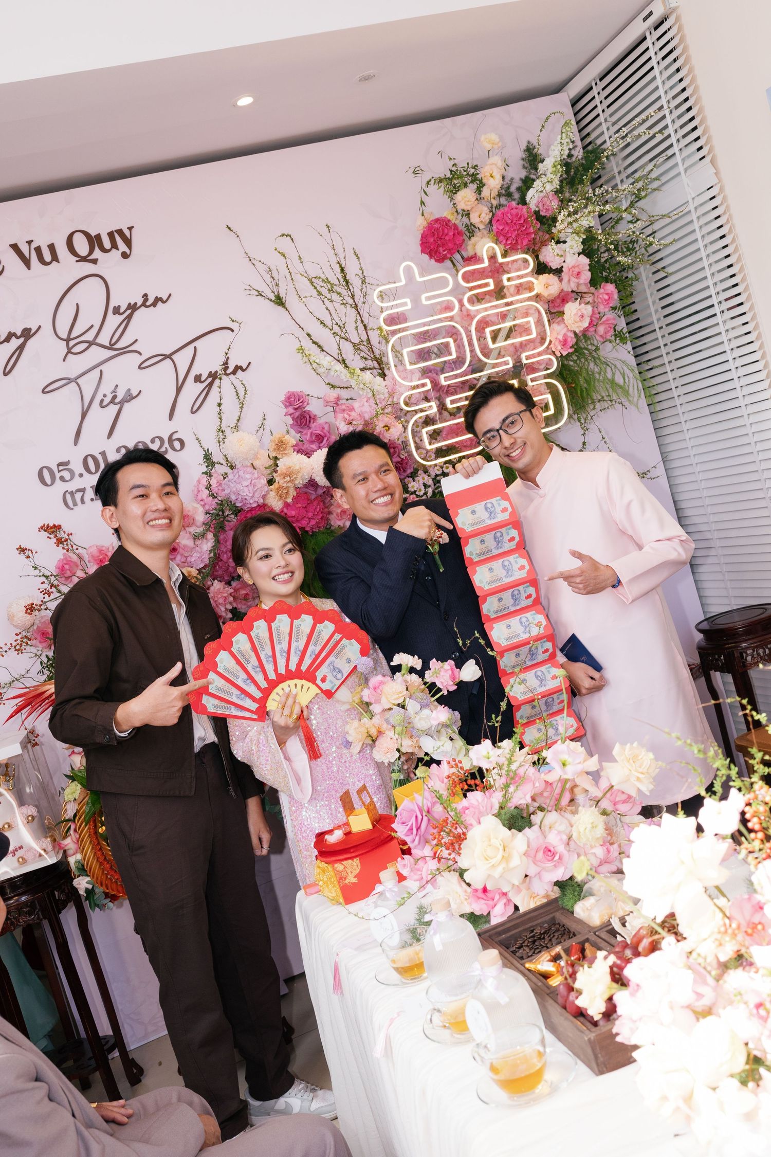 Vietnamese wedding couple posing with guests near floral decorations and double happiness symbol.