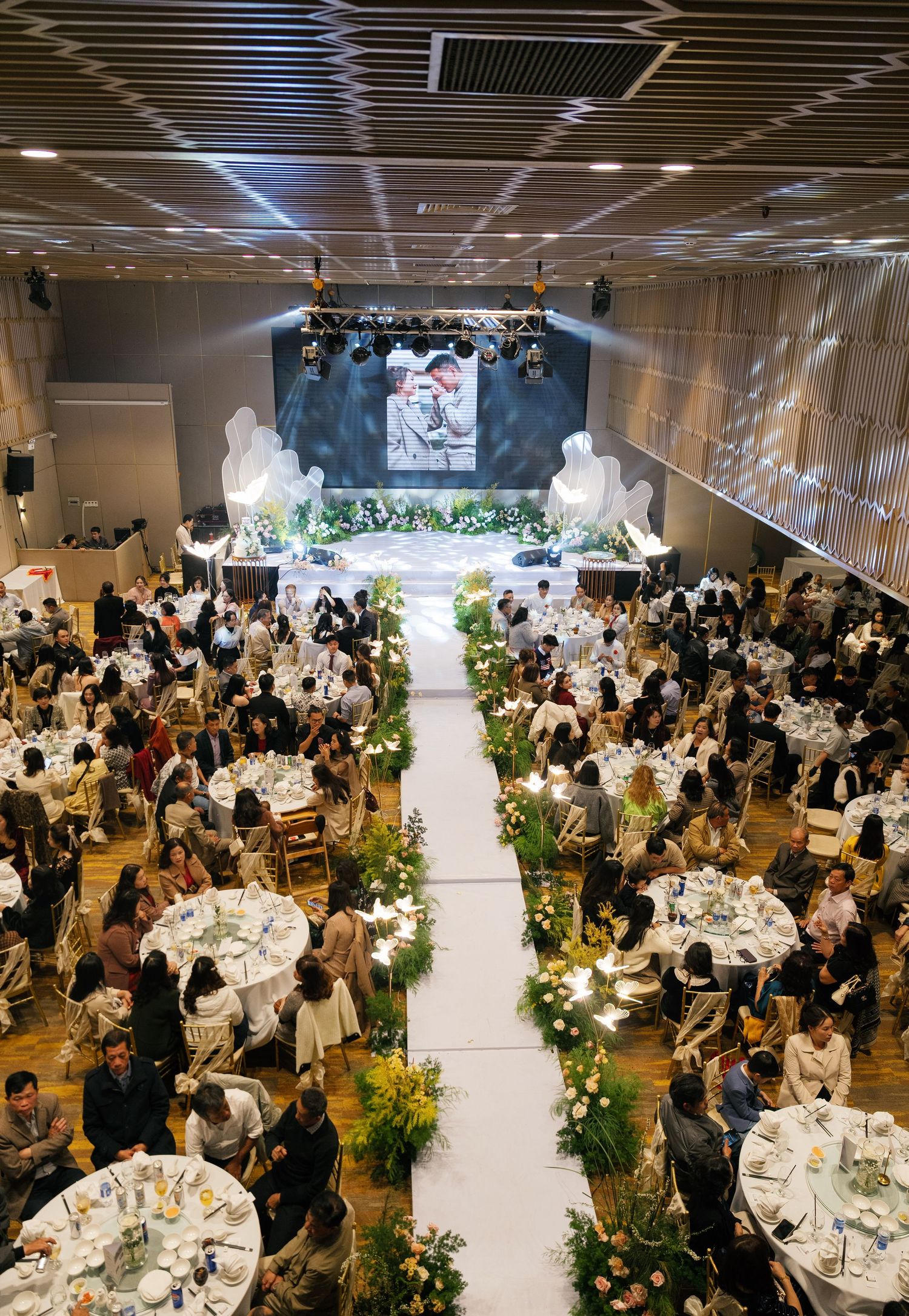 Elegant Vietnamese wedding banquet hall with long aisle, round tables, and large screen displaying couple.