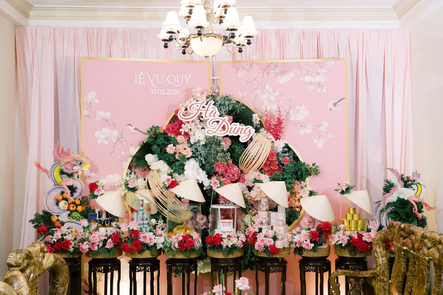 Vietnamese wedding backdrop with pink floral arrangement, traditional non la hats, and colorful flowers on decorated table.