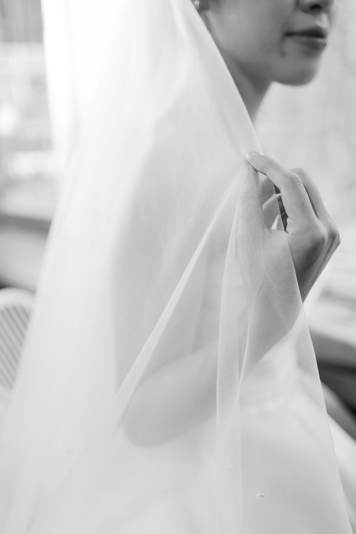 Close-up black and white photo of bride holding delicate white wedding veil with both hands.