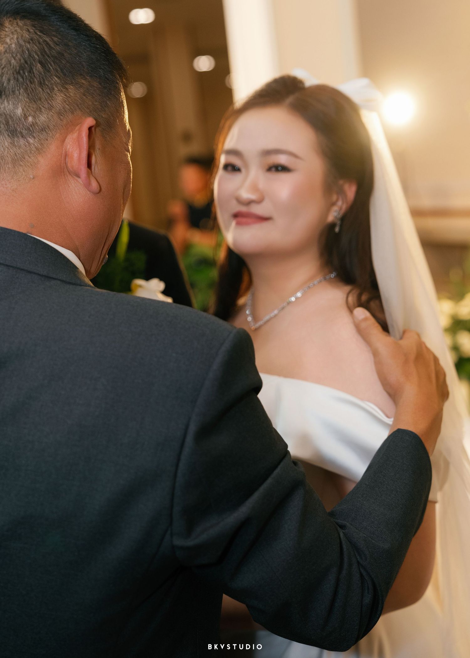 Bride in white gown and veil smiles at groom during wedding ceremony dance at elegant venue.
