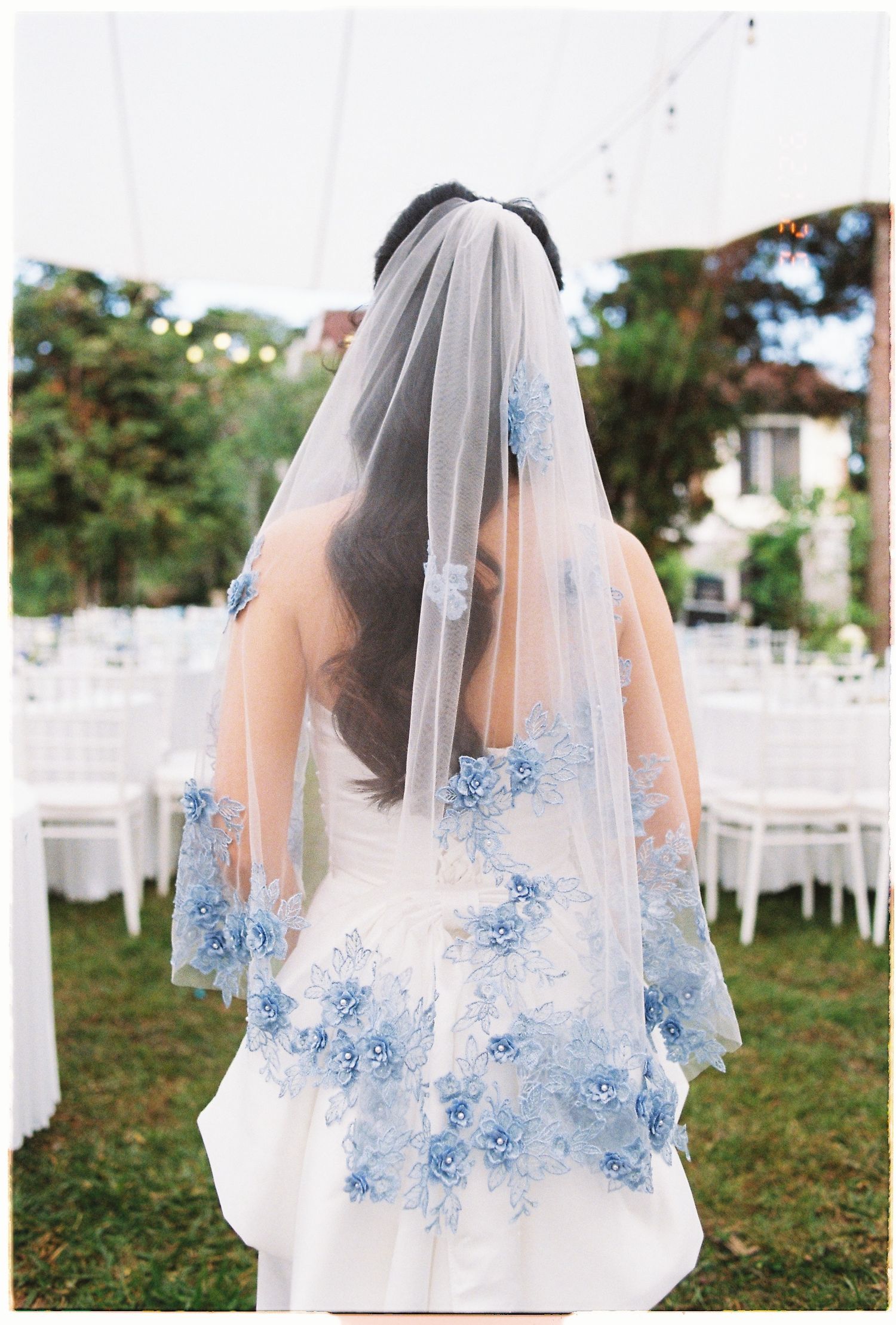 Bride wearing a white wedding dress with blue floral lace veil at an outdoor garden wedding reception.