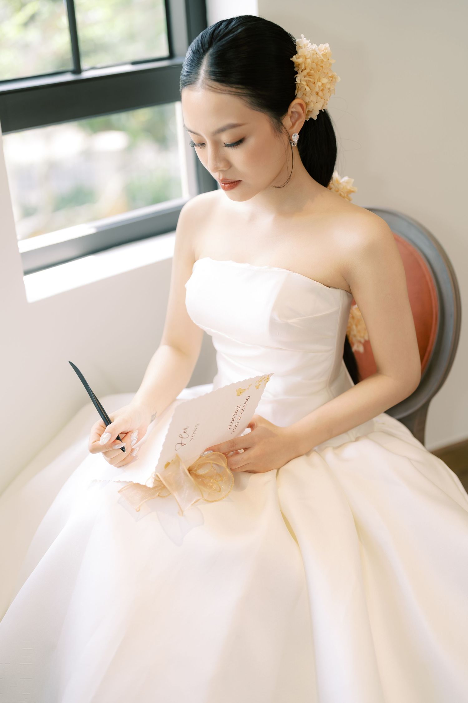 Beautiful bride in strapless white ball gown writing vows with yellow flowers in hair.