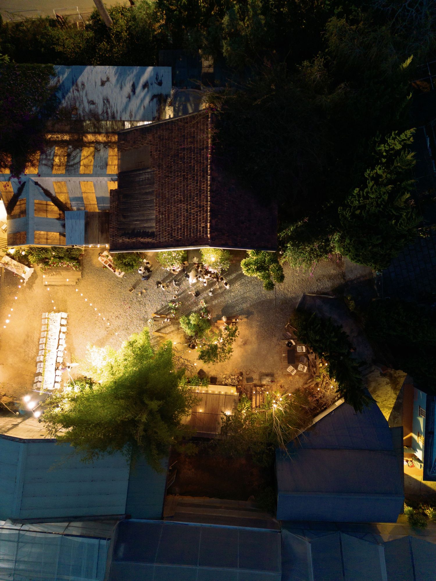 Aerial night view of illuminated outdoor restaurant courtyard surrounded by trees and buildings.