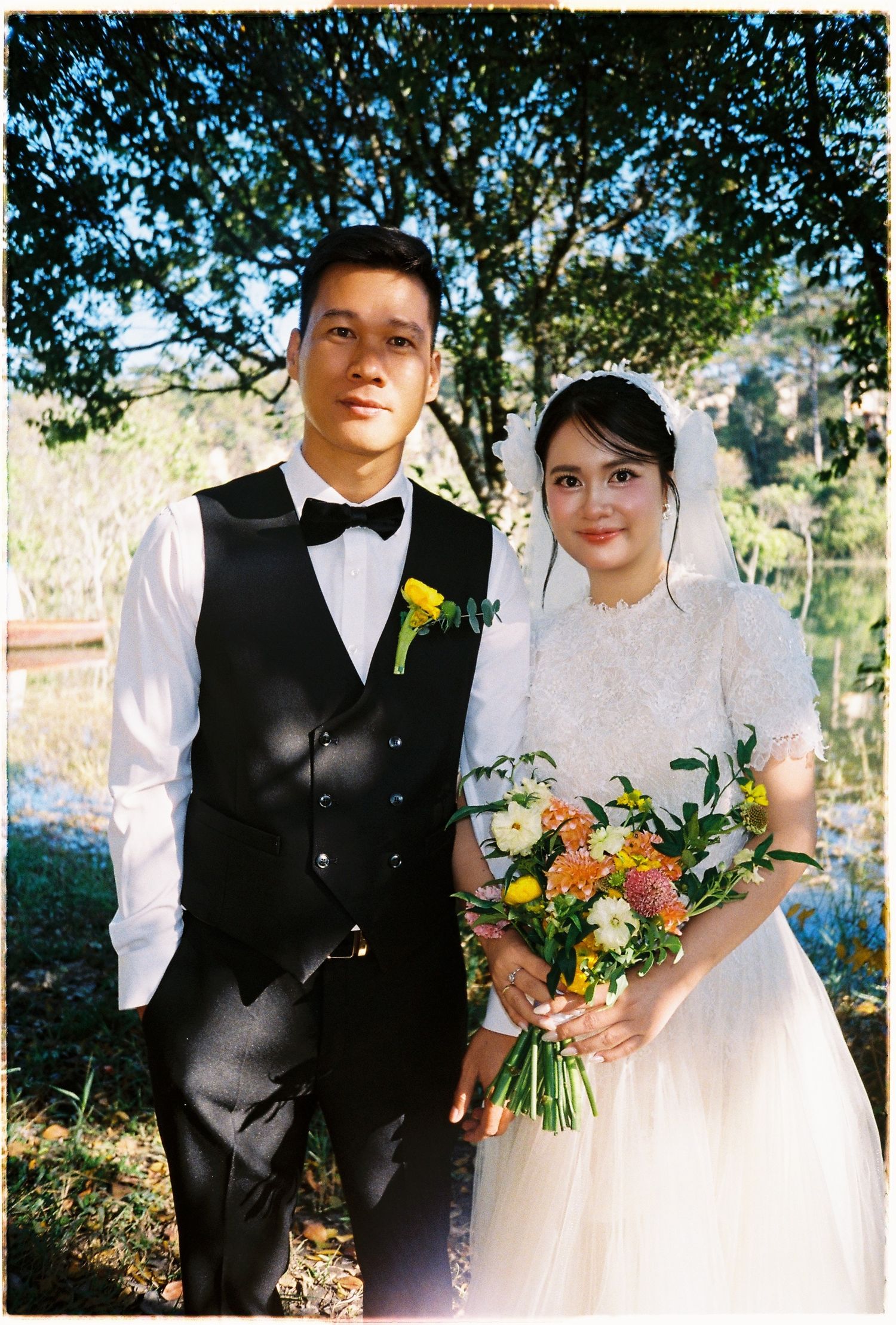 Bride and groom pose together outdoors in film photo style, bride holding colorful mixed bouquet.
