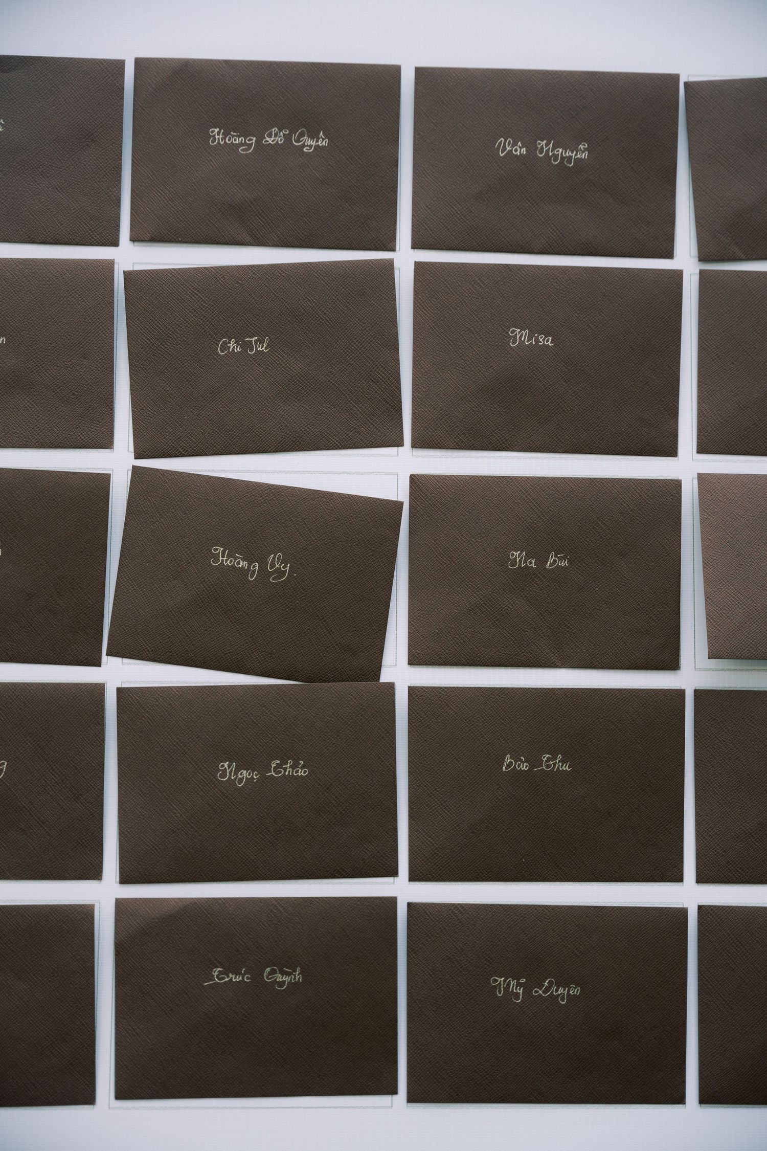 Dark brown envelope place cards with white calligraphy handwriting arranged on a white surface.