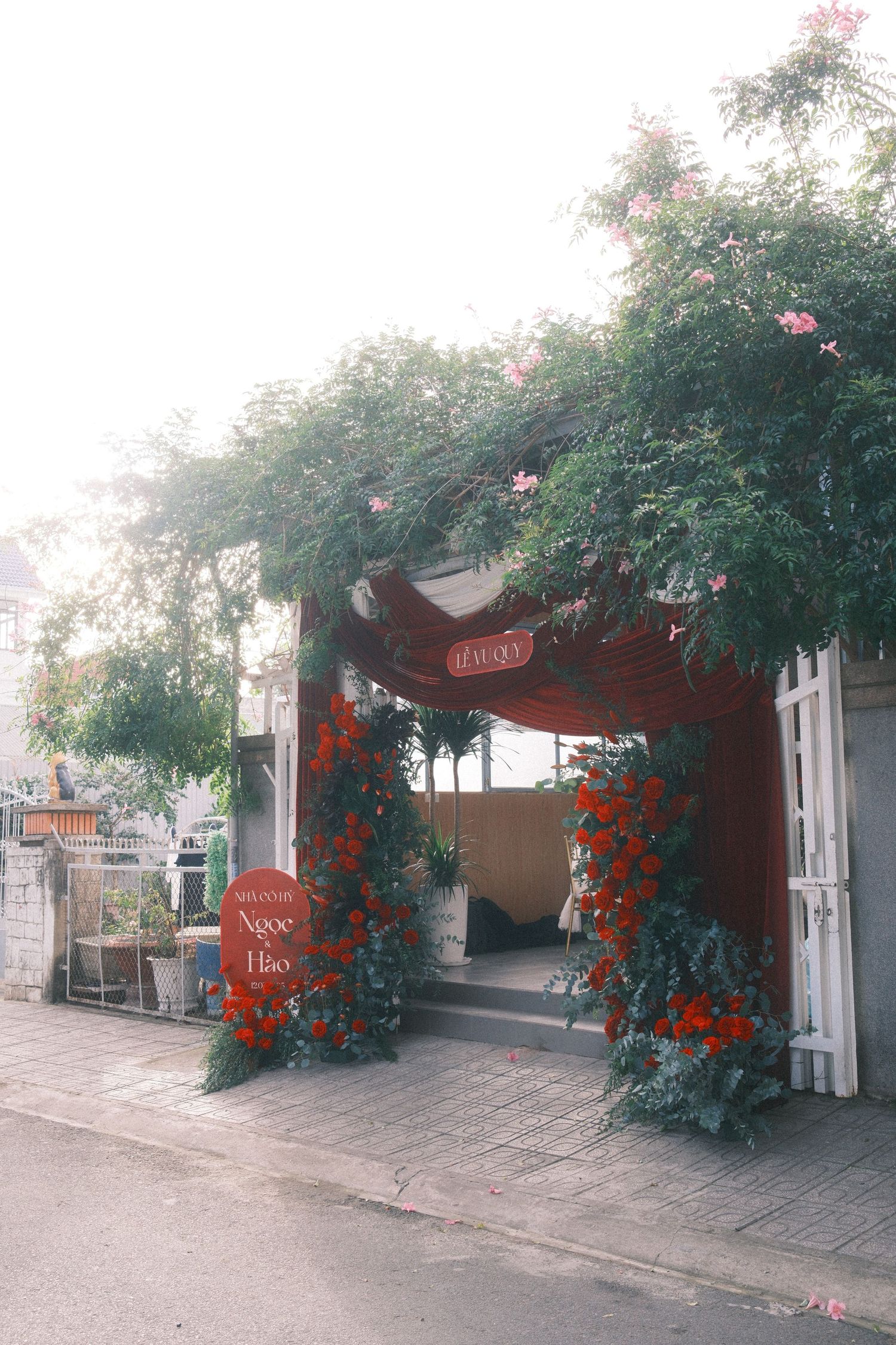 Floral archway entrance decorated with red flowers and lush greenery at a Vietnamese wedding venue.